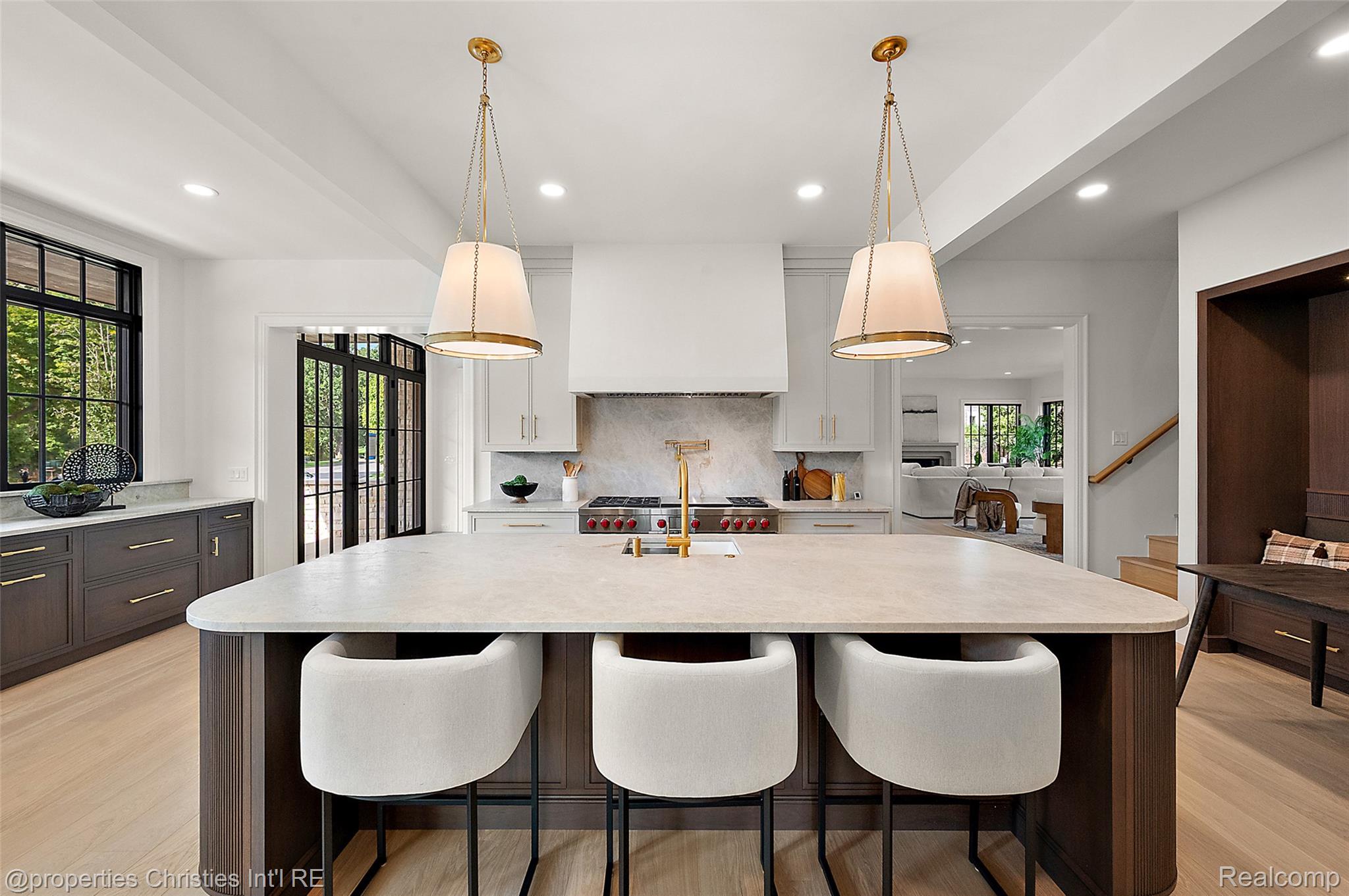Bright kitchen with a large stone island, three upholstered stools, and a professional range.