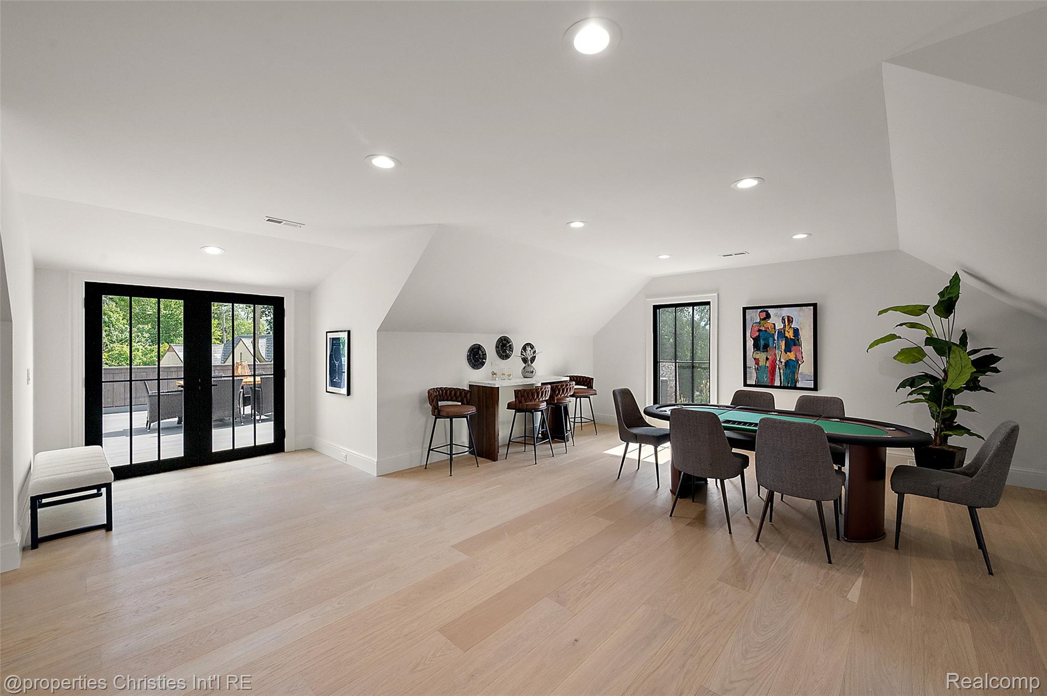 Upstairs game room with a green pool table, bar seating, and black-framed doors to a deck.