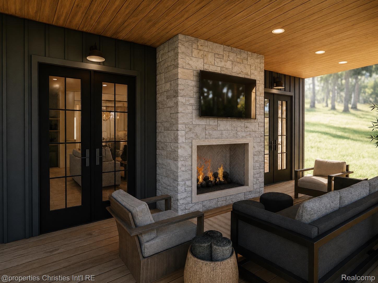 Covered patio with a stone fireplace, television, dark-framed glass doors, and cushioned seating overlooking a lawn.