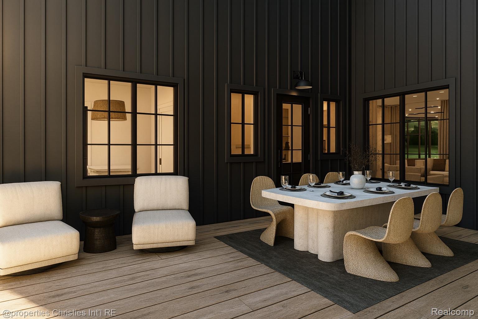 Outdoor dining patio with a stone table, woven chairs, and cream lounge seating beside dark siding.