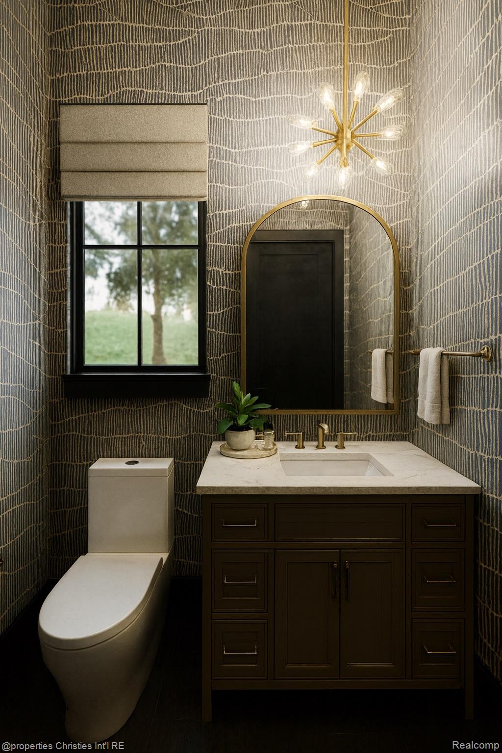 Bathroom with dark wood vanity, arched gold-framed mirror, patterned wallpaper, and a starburst light fixture.