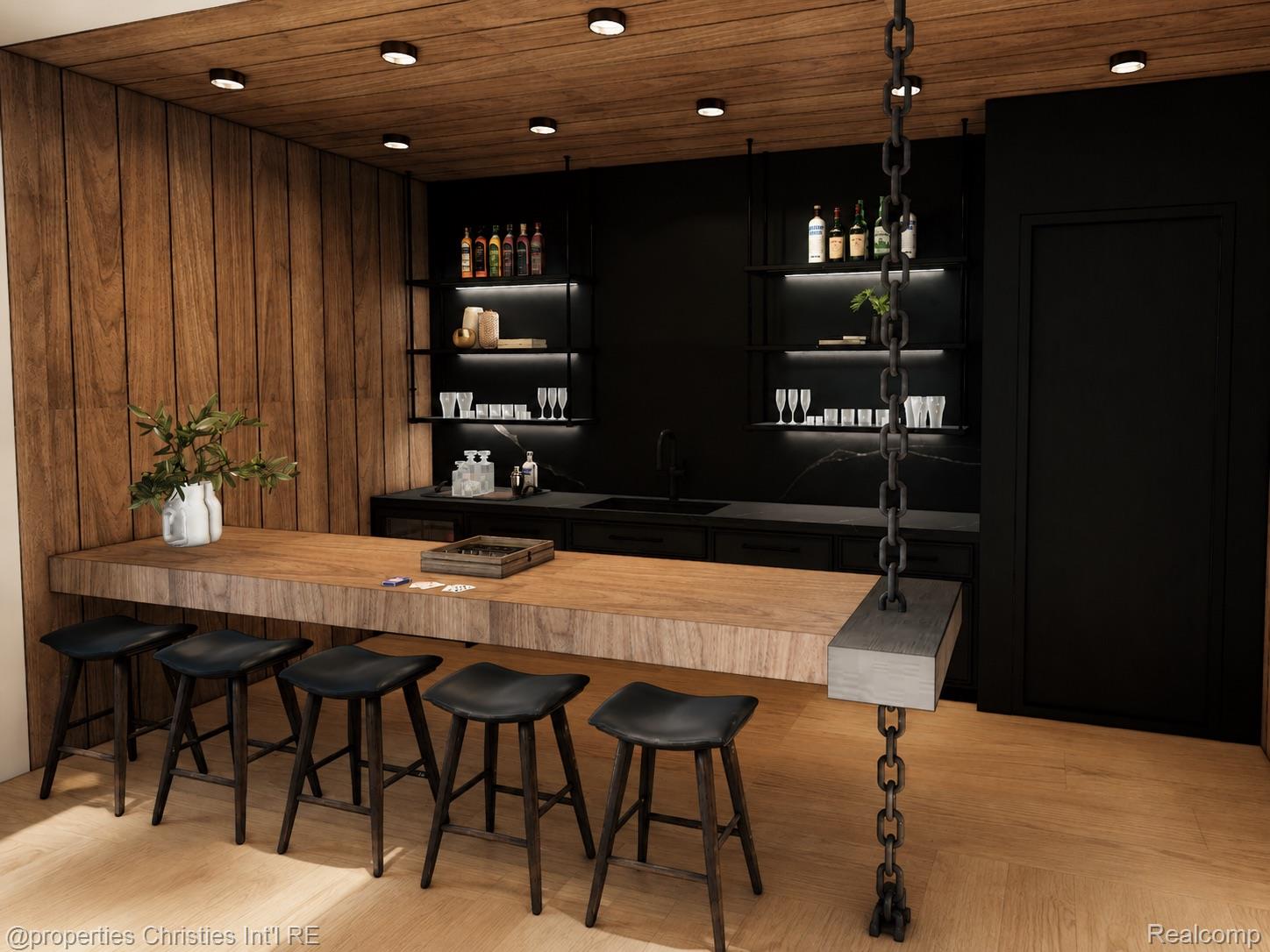 Wet bar with a long wood counter, black stools, dark cabinetry, and backlit shelves.