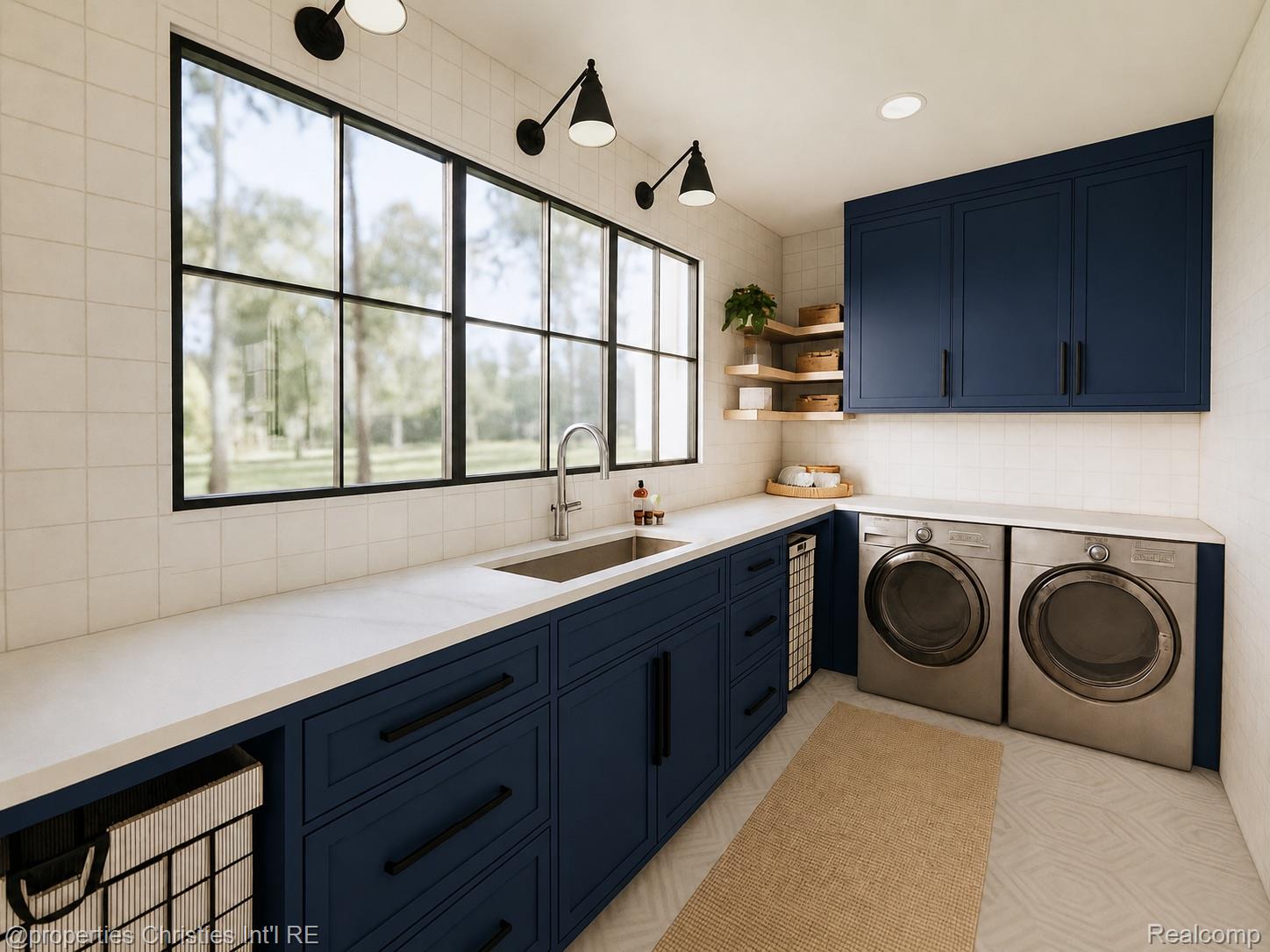Laundry room with navy cabinetry, white tile, large windows, and stainless front-loading washer and dryer.