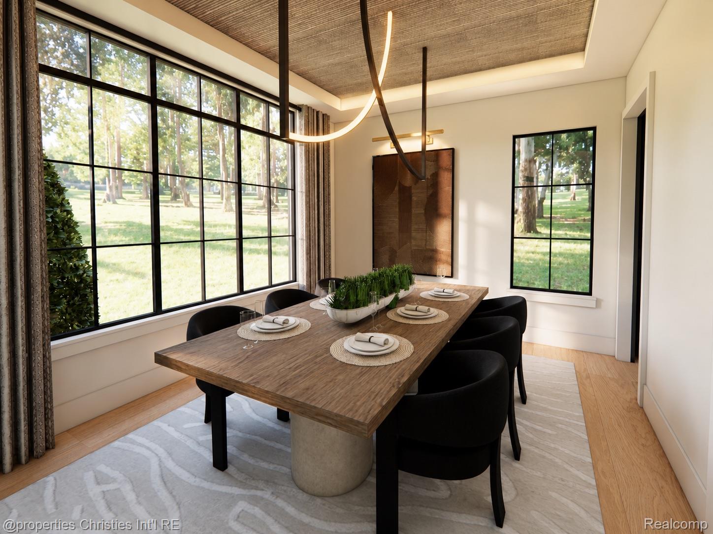 Dining room with a long wood table and black chairs beside large windows overlooking a tree-lined lawn.