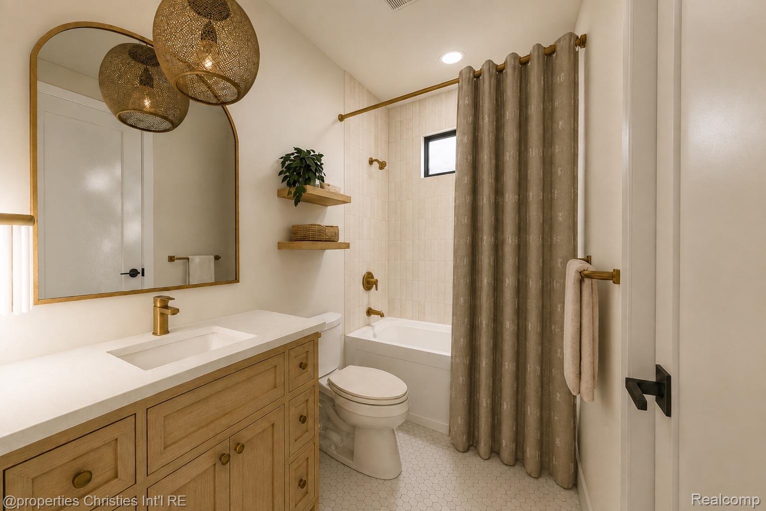 Bathroom with a light wood vanity, brass fixtures, arched mirror, and tub with a taupe curtain.