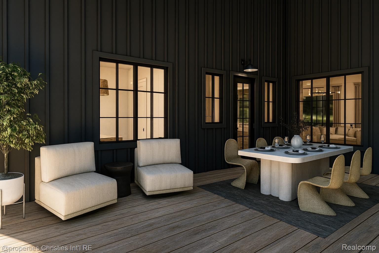 Furnished patio with a dining table and lounge chairs against dark siding and glowing windows.