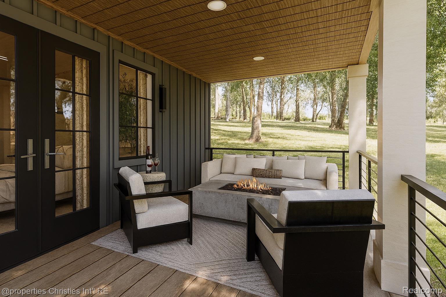 Covered porch with cushioned seating around a gas fire table, overlooking a tree-lined lawn.