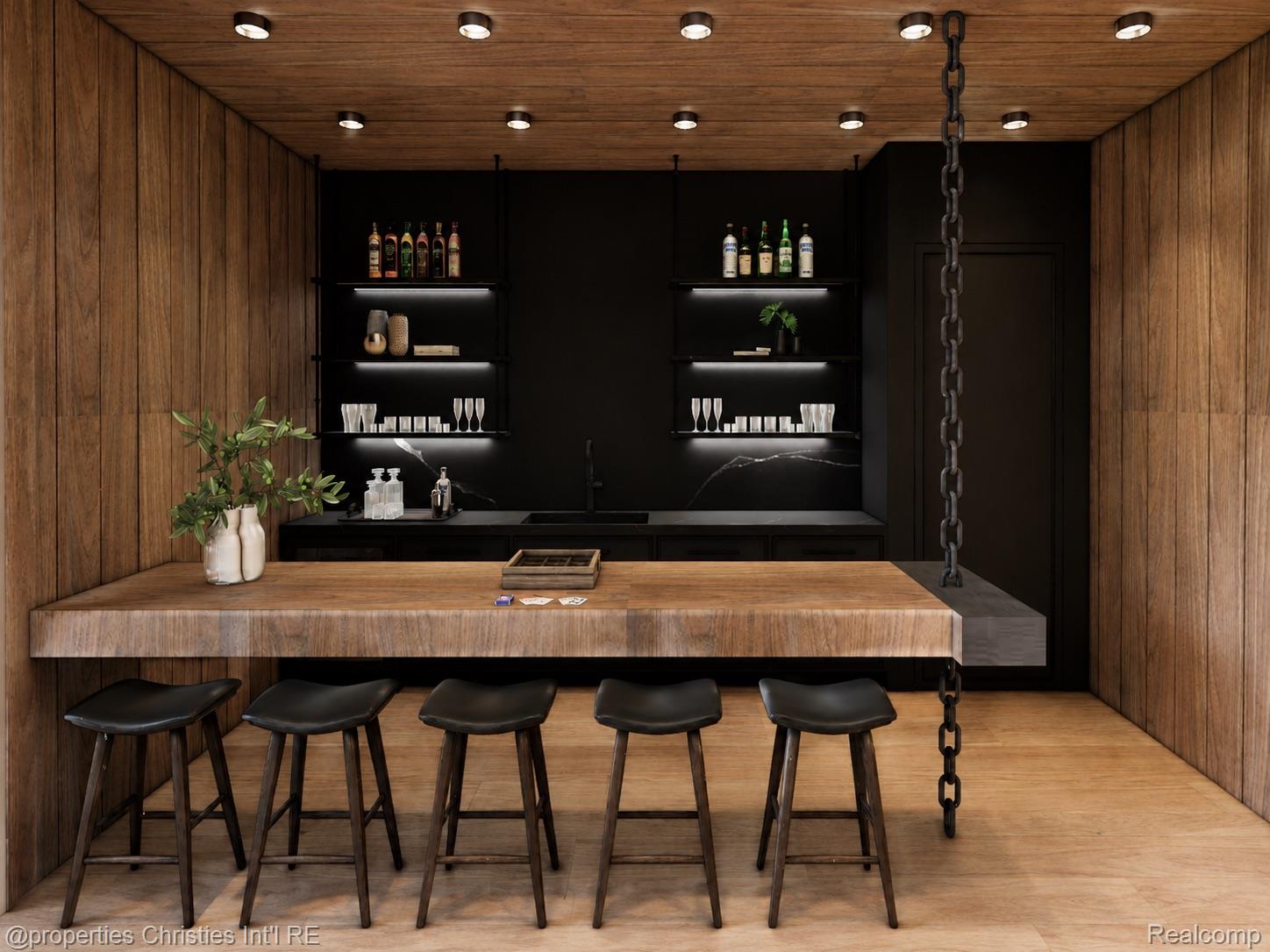 Wood-paneled home bar with a thick counter, five black stools, and illuminated shelves of bottles and glassware.