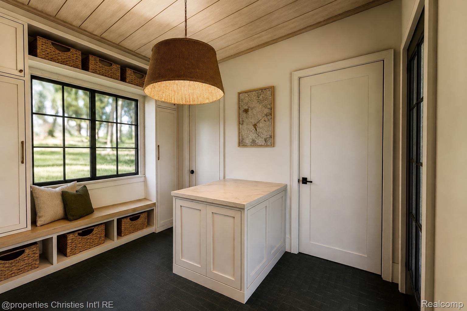 Mudroom with a built-in window bench, woven baskets, cream cabinetry, and a central island.