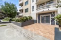 Residential building entrance with balconies, a paved walkway, and landscaped planters.