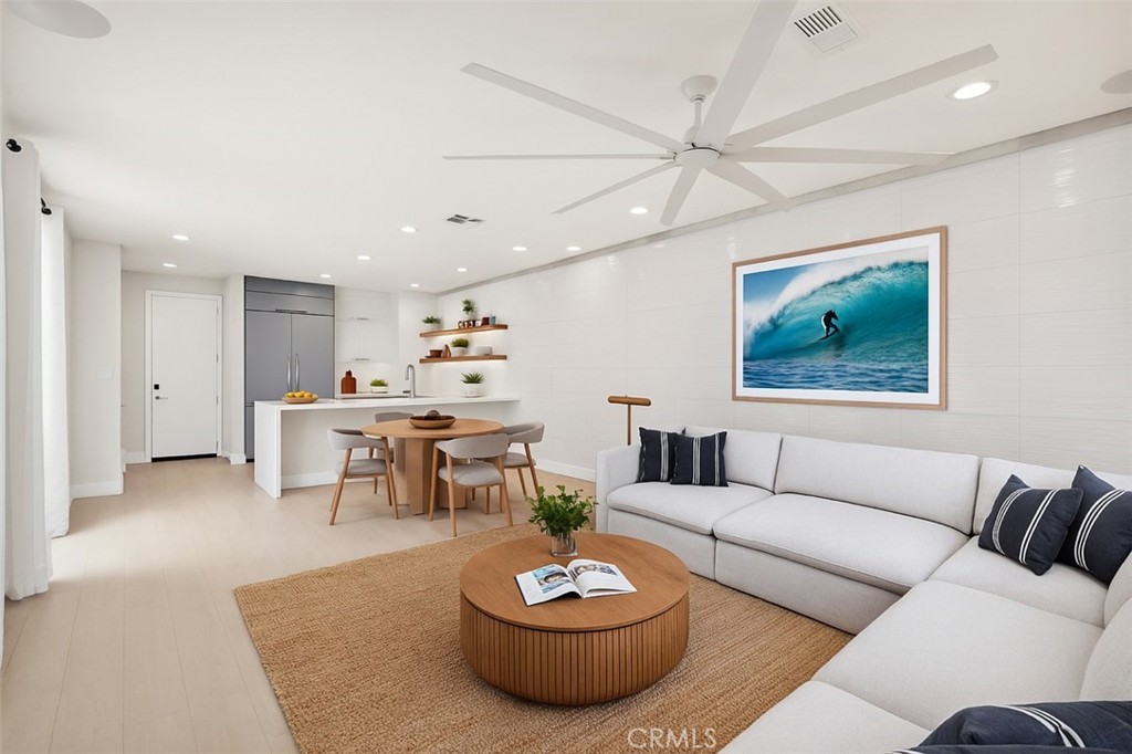 Open-plan living room with a white sectional, round wood coffee table, and dining area.