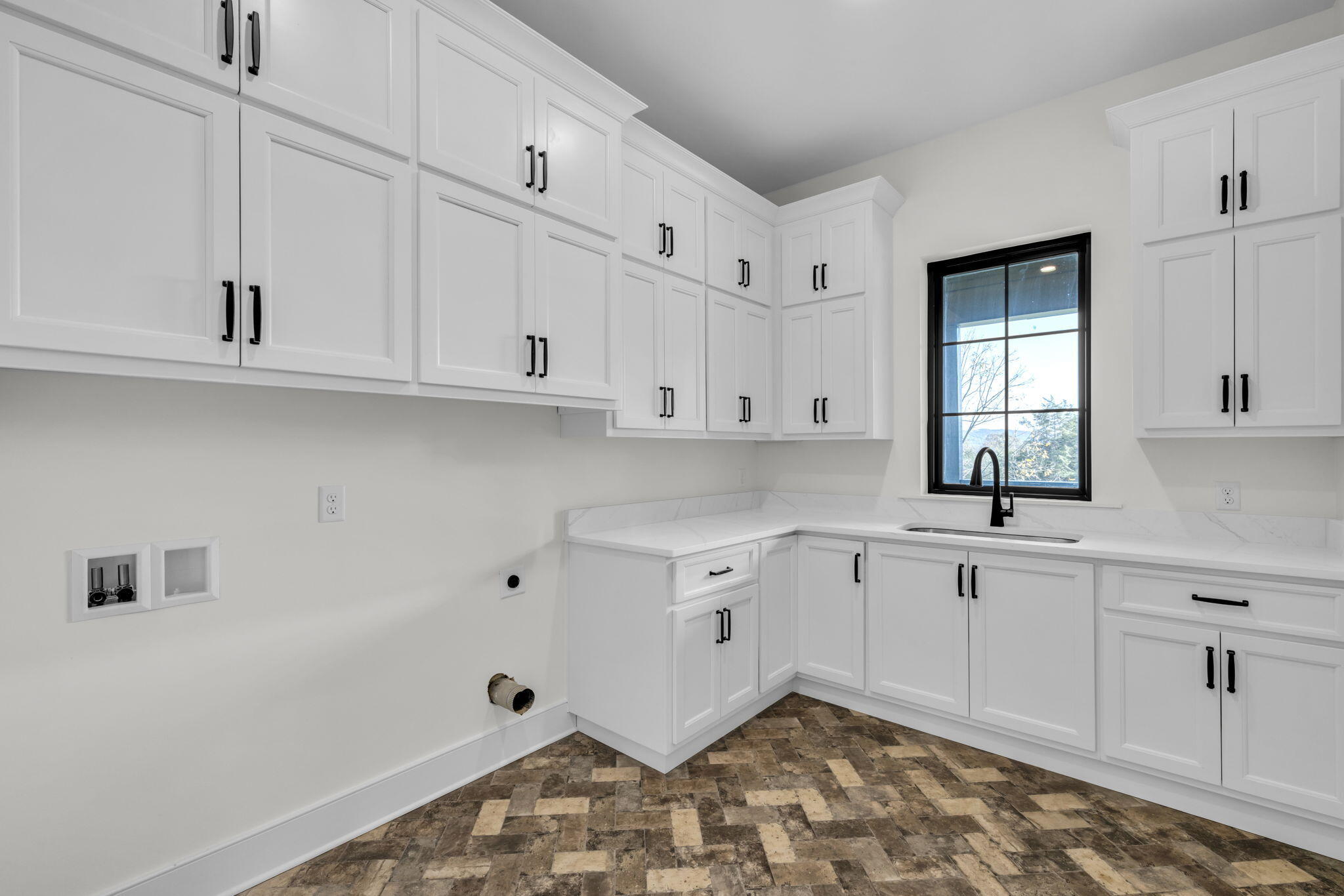 Kitchen with white Shaker cabinets, black hardware, a window over the sink, and patterned tile flooring.