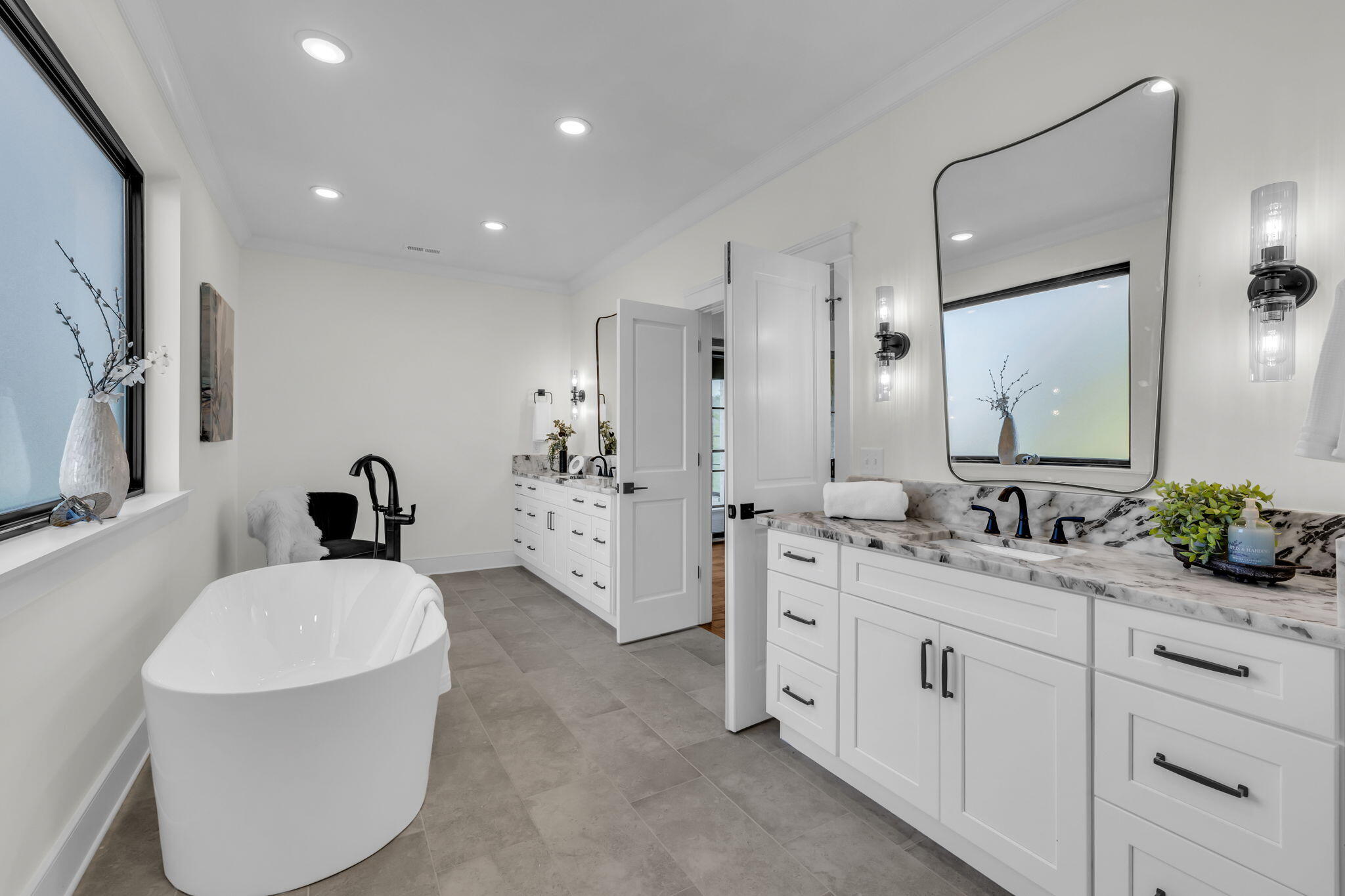 Bathroom with a freestanding soaking tub and double vanity with marble counters and black fixtures.