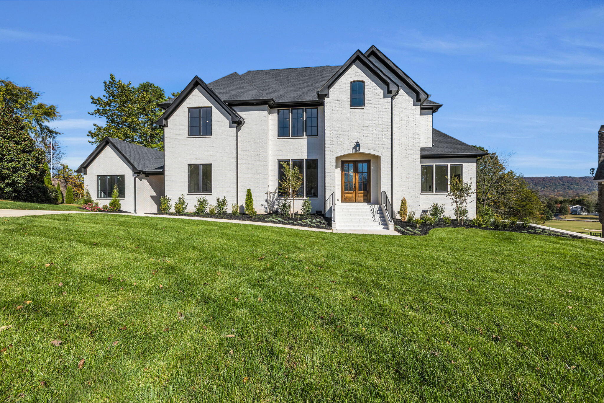 Two-story white brick house with dark gables, wood entry doors, and a broad green lawn.