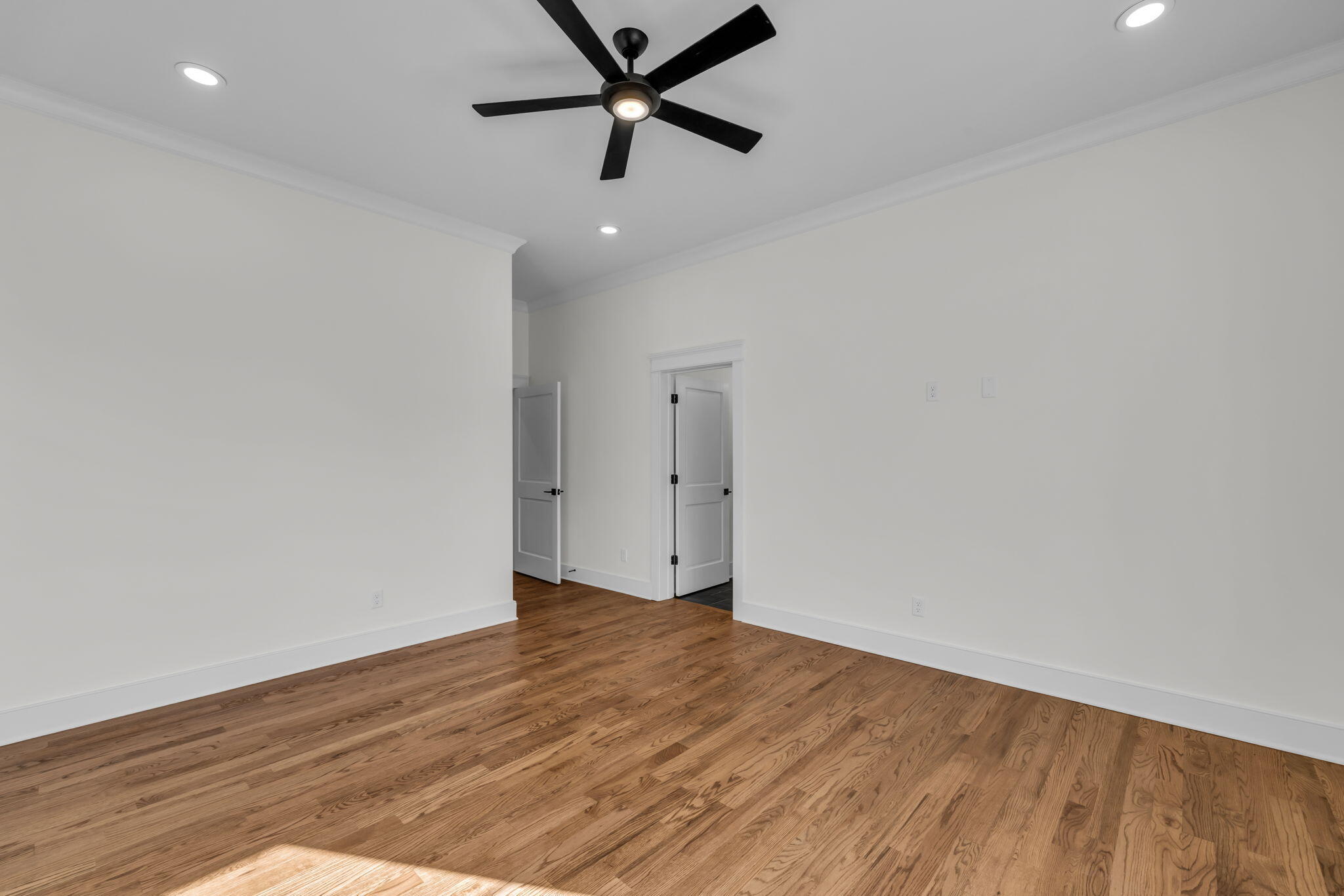 Empty room with hardwood floors, white walls, and a black ceiling fan with a light.