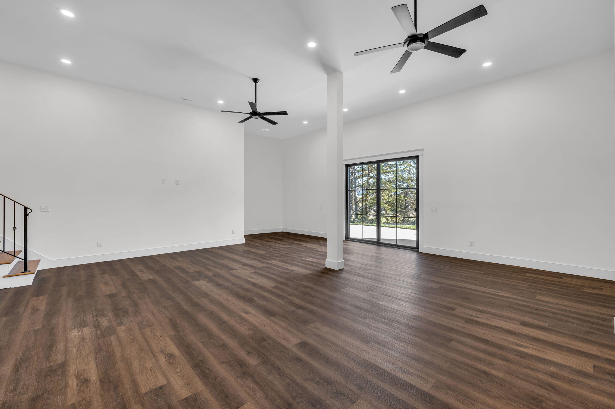 Vacant open-plan living area with dark flooring, two ceiling fans, and sliding glass doors to a patio.