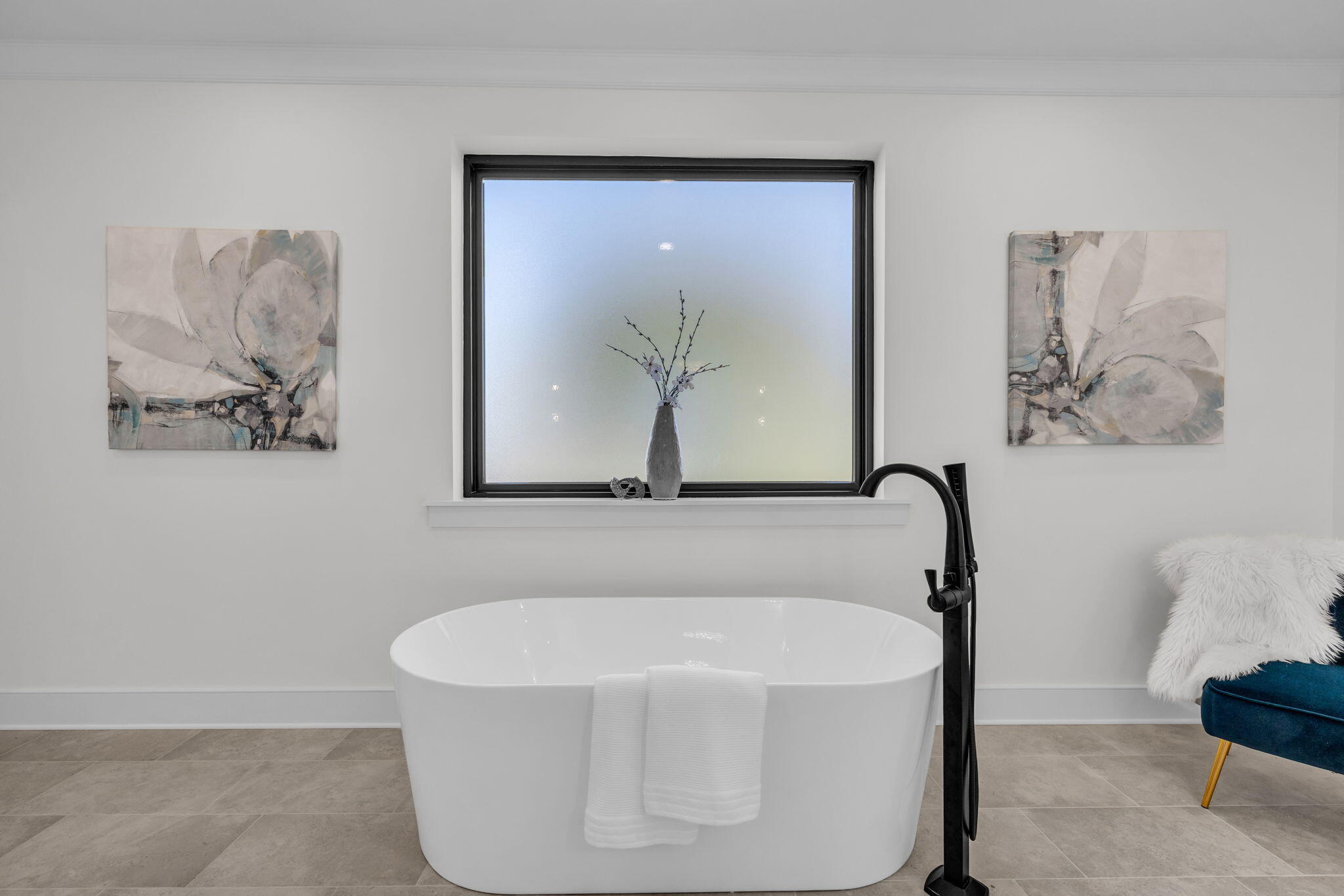 Bathroom with a freestanding white tub beneath a large window and a black floor-mounted faucet.