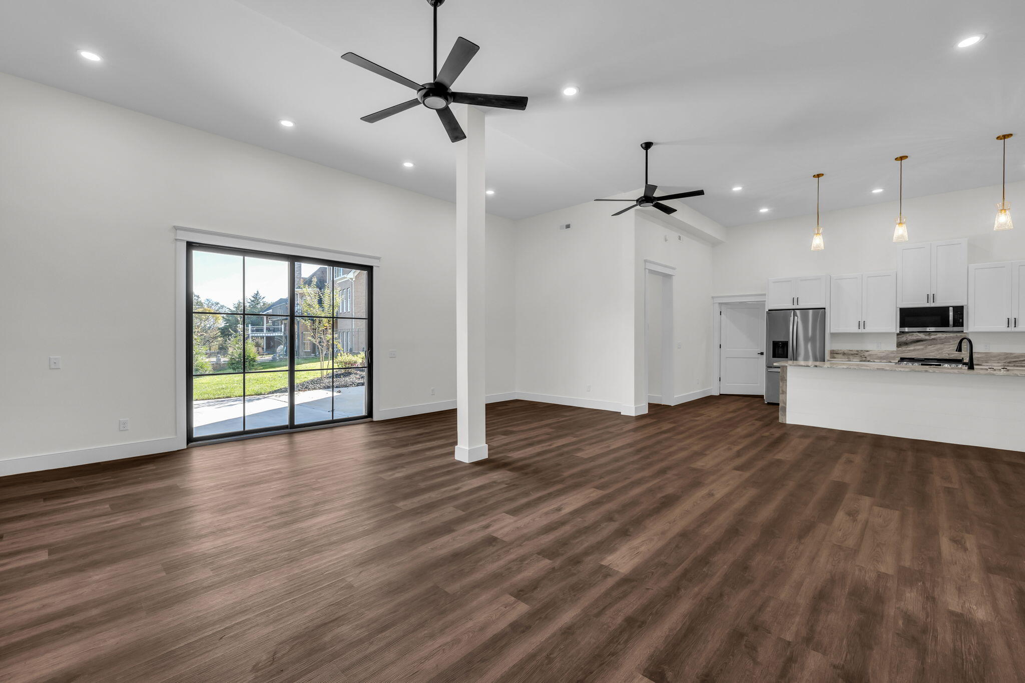 Open living area and kitchen with dark wood floors, white cabinetry, and a sliding glass door to the patio.