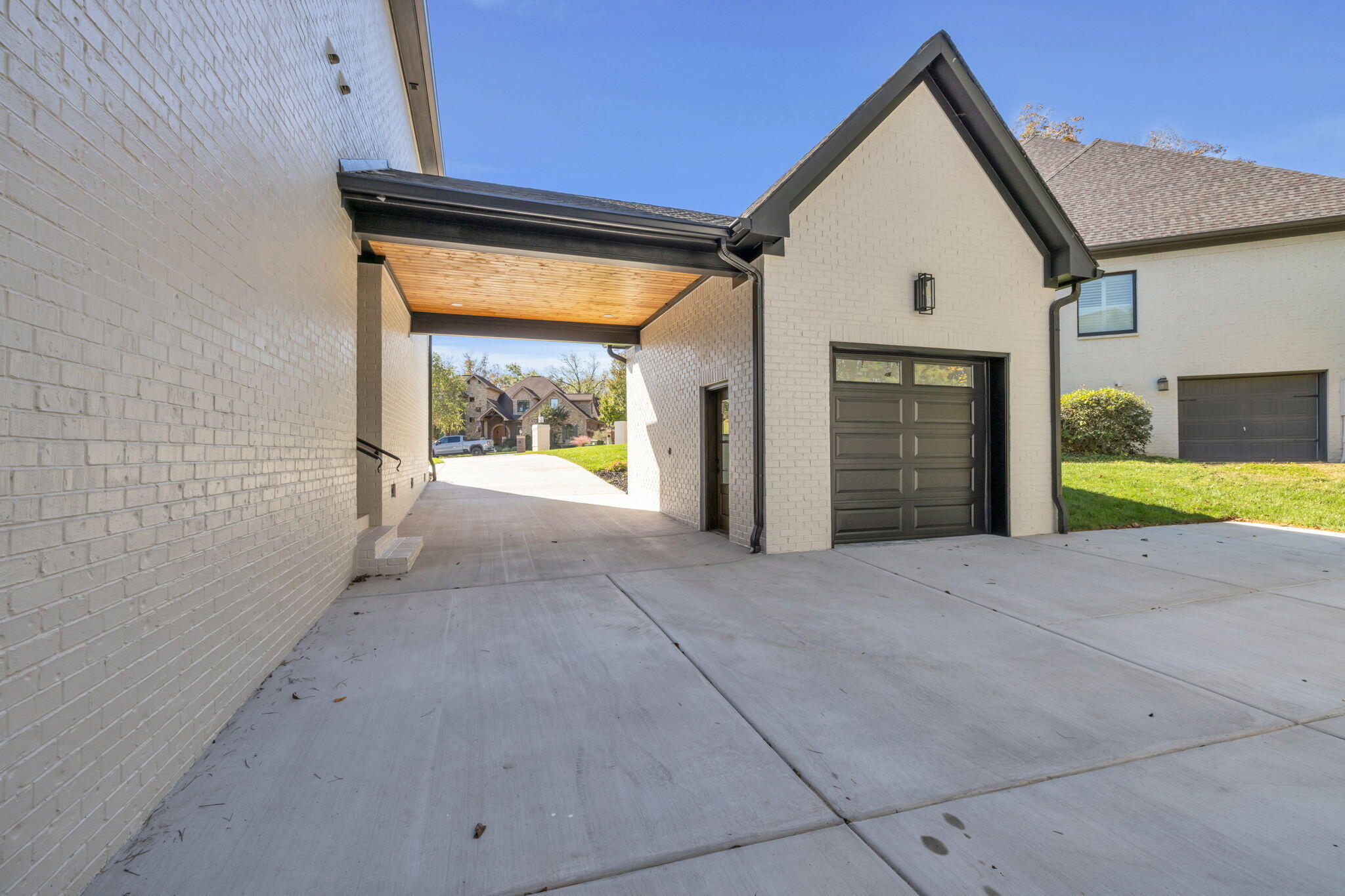 Home exterior with a covered drive-through breezeway, wood-paneled ceiling, and dark garage door.