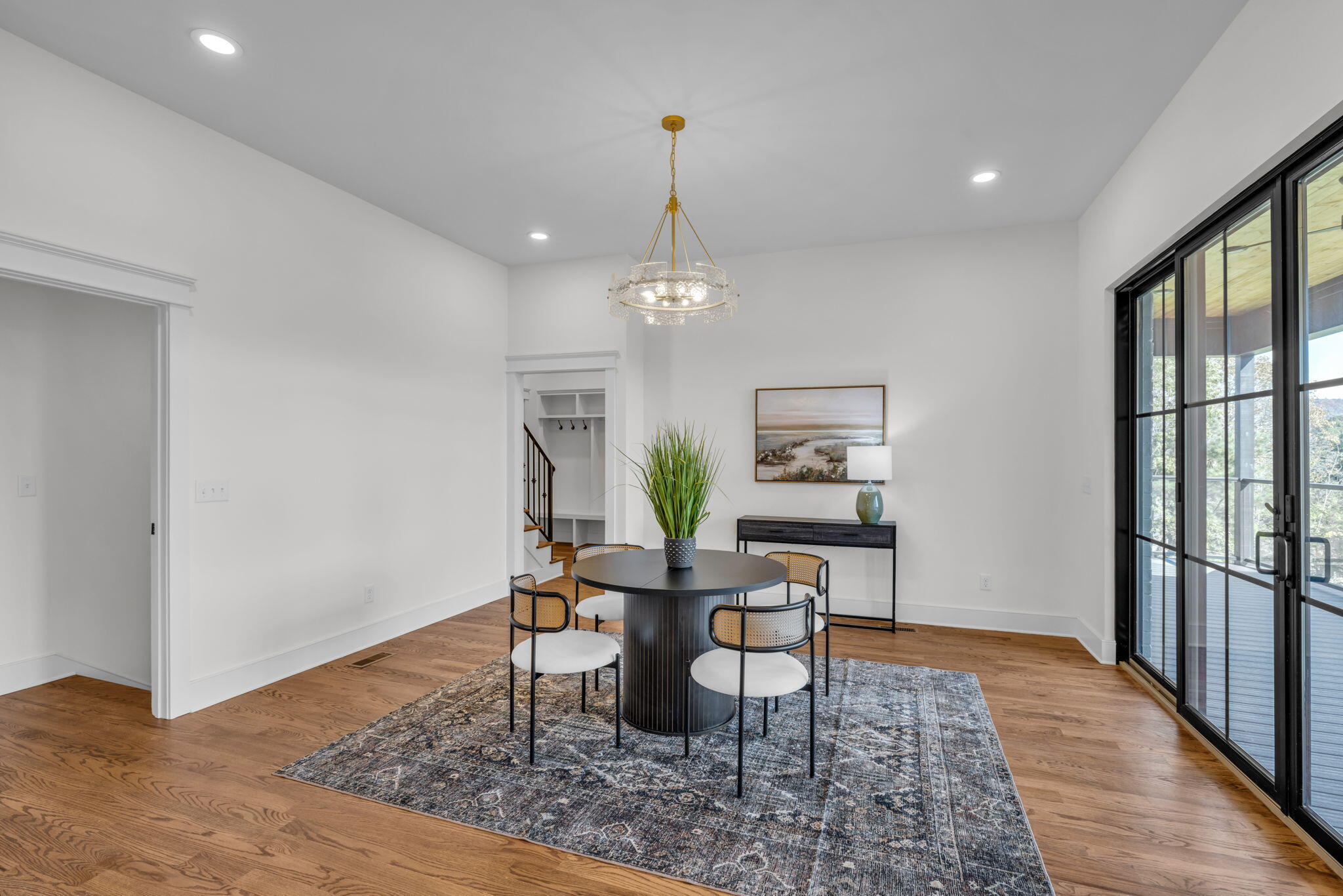 Staged dining room with a round table, gold chandelier, and black-framed glass doors.