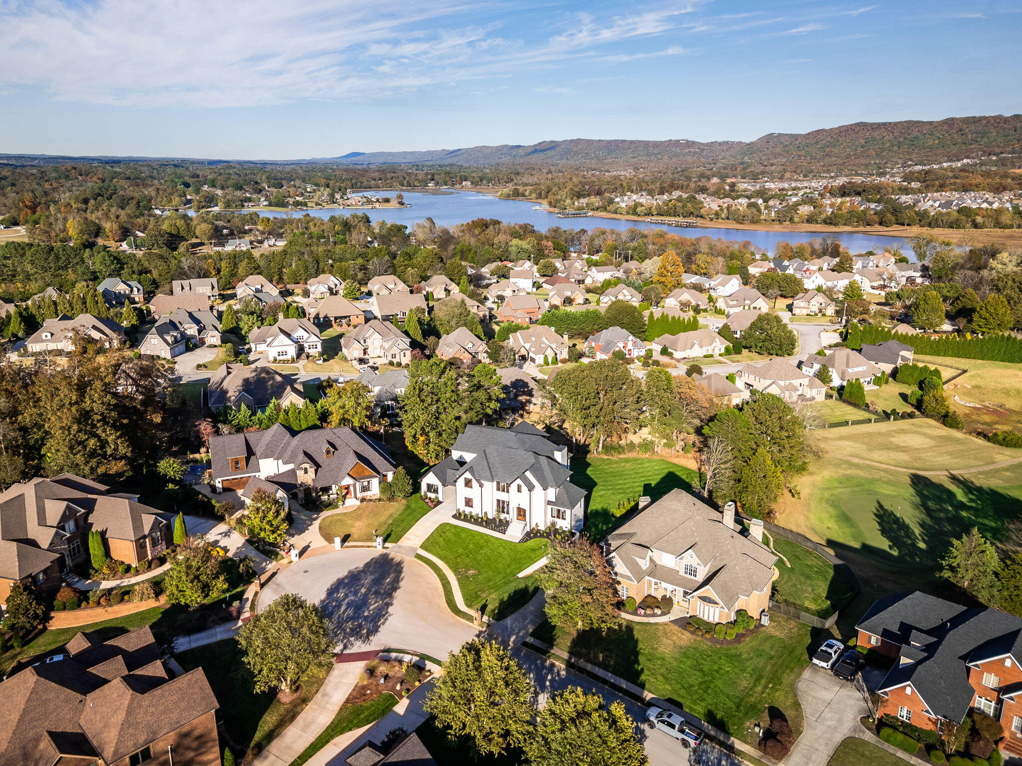 Aerial view of a residential neighborhood beside a lake, with autumn trees and wooded hills.