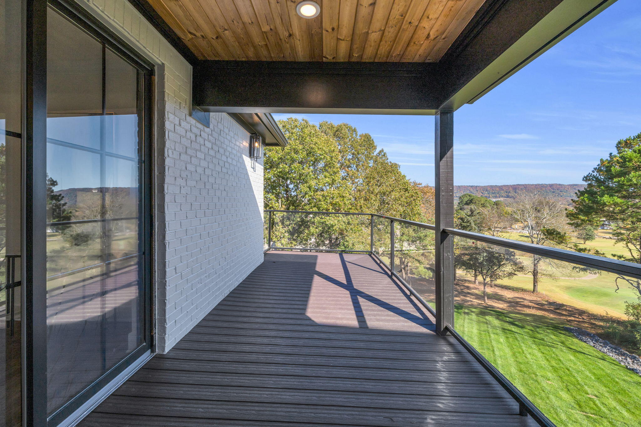 Covered balcony with glass railings and wooded hills beyond the landscaped grounds.