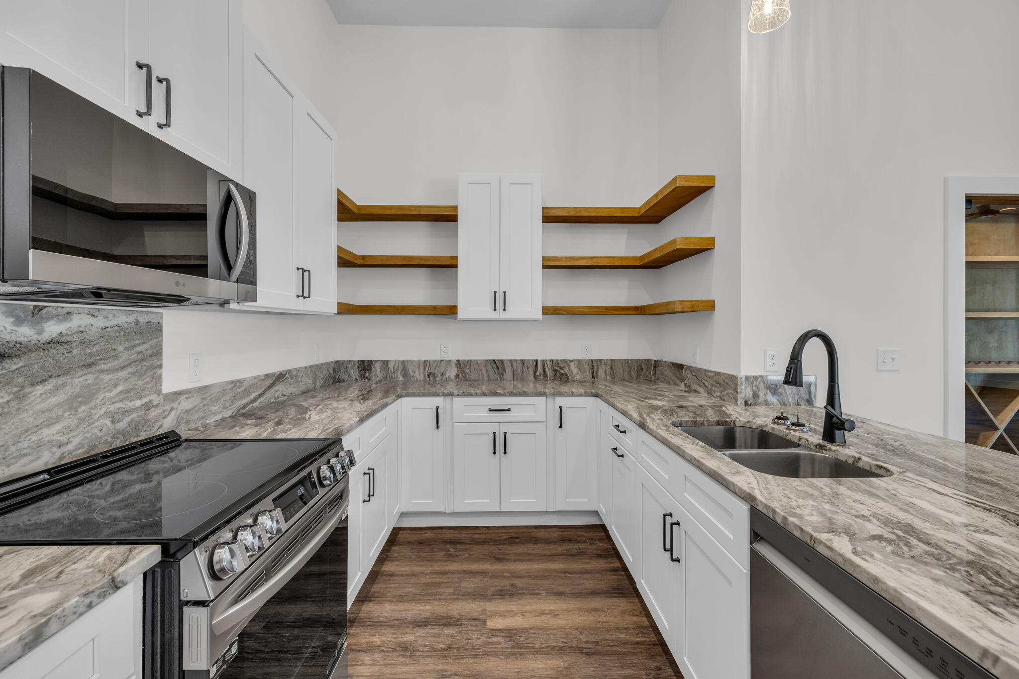 Modern kitchen with white cabinets, veined stone counters, open wood shelves, and stainless-steel appliances.