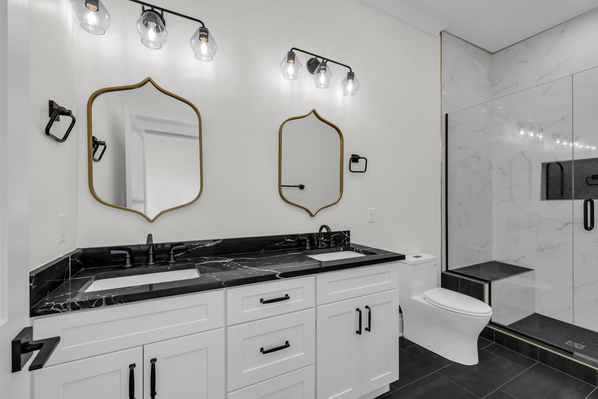Modern bathroom with a double vanity, gold-framed mirrors, and a glass-enclosed shower.