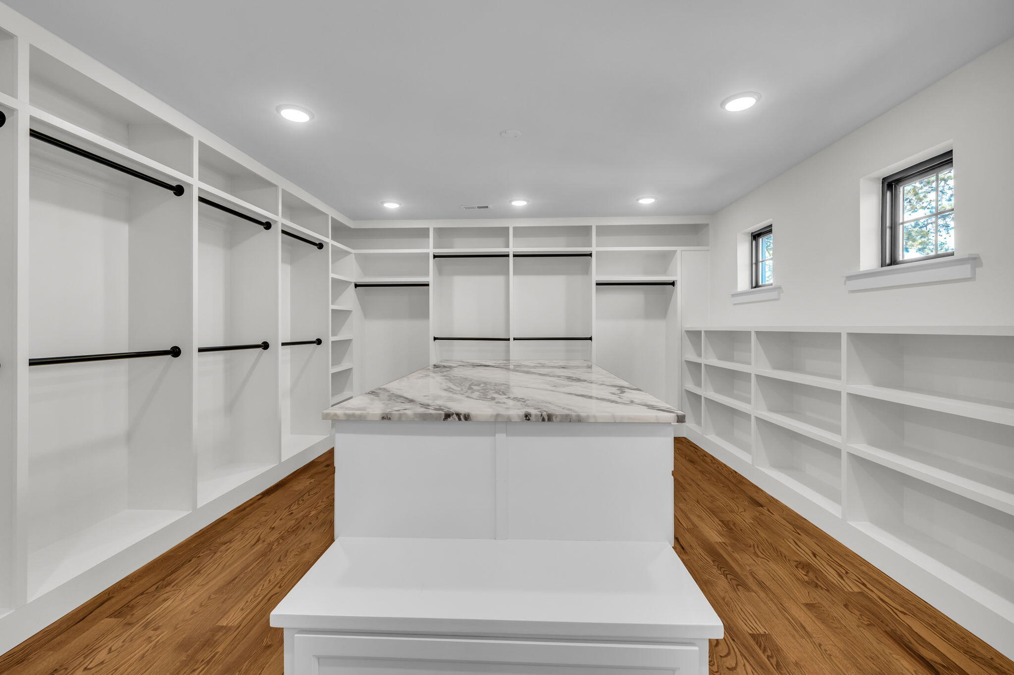 Walk-in closet with extensive white built-ins, a marble-top island, and wood flooring.