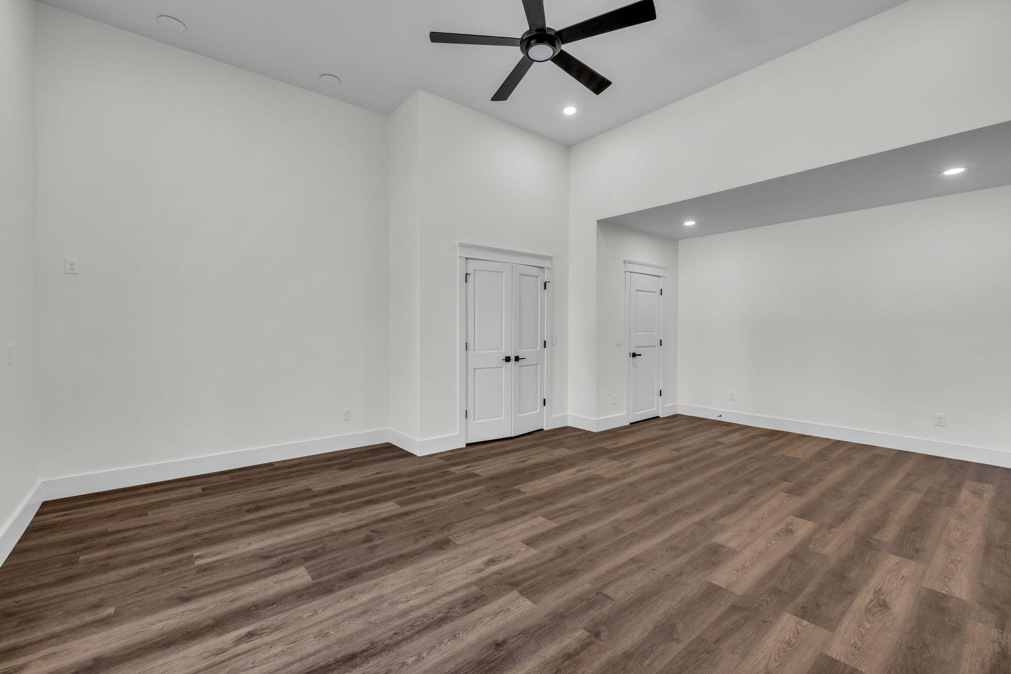 Empty room with dark wood-look flooring, a black ceiling fan, and two white doors.