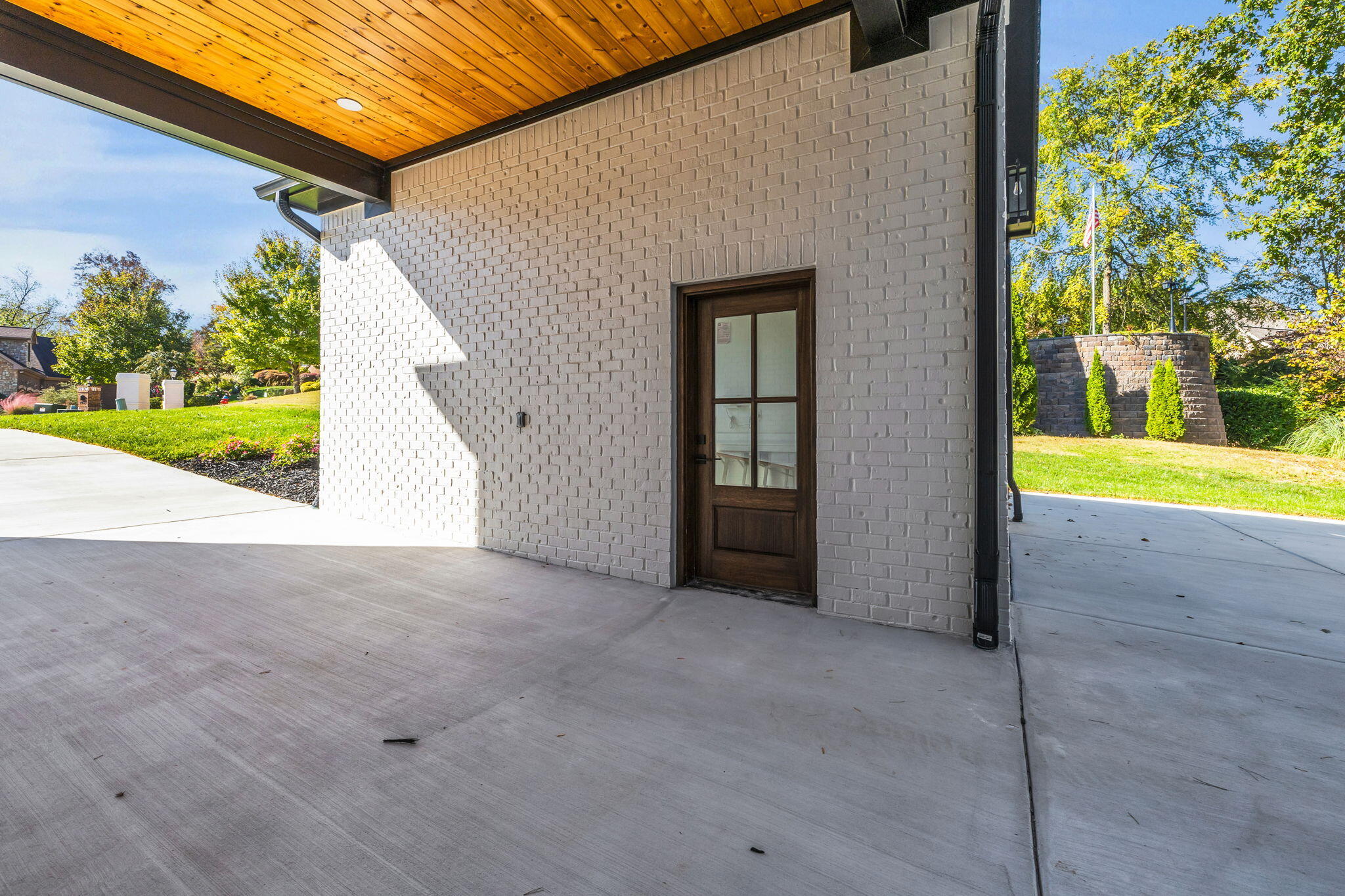 Covered concrete patio with a wood-plank ceiling and dark-framed glass entry door.