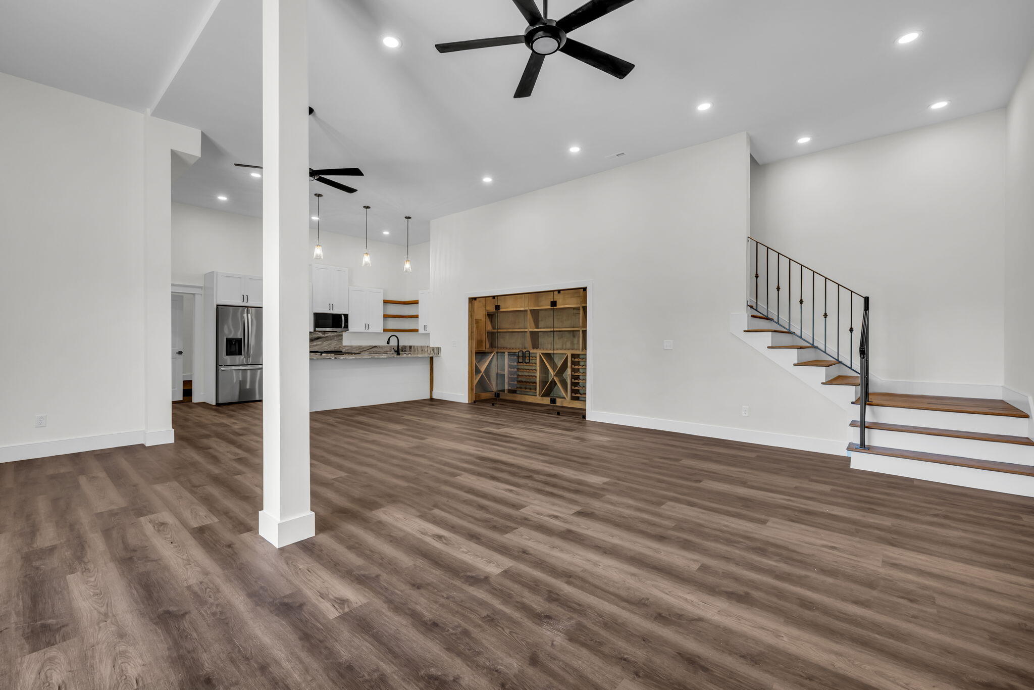 Open living area with wood-look floors, kitchen, built-in wine cabinet, and open staircase.