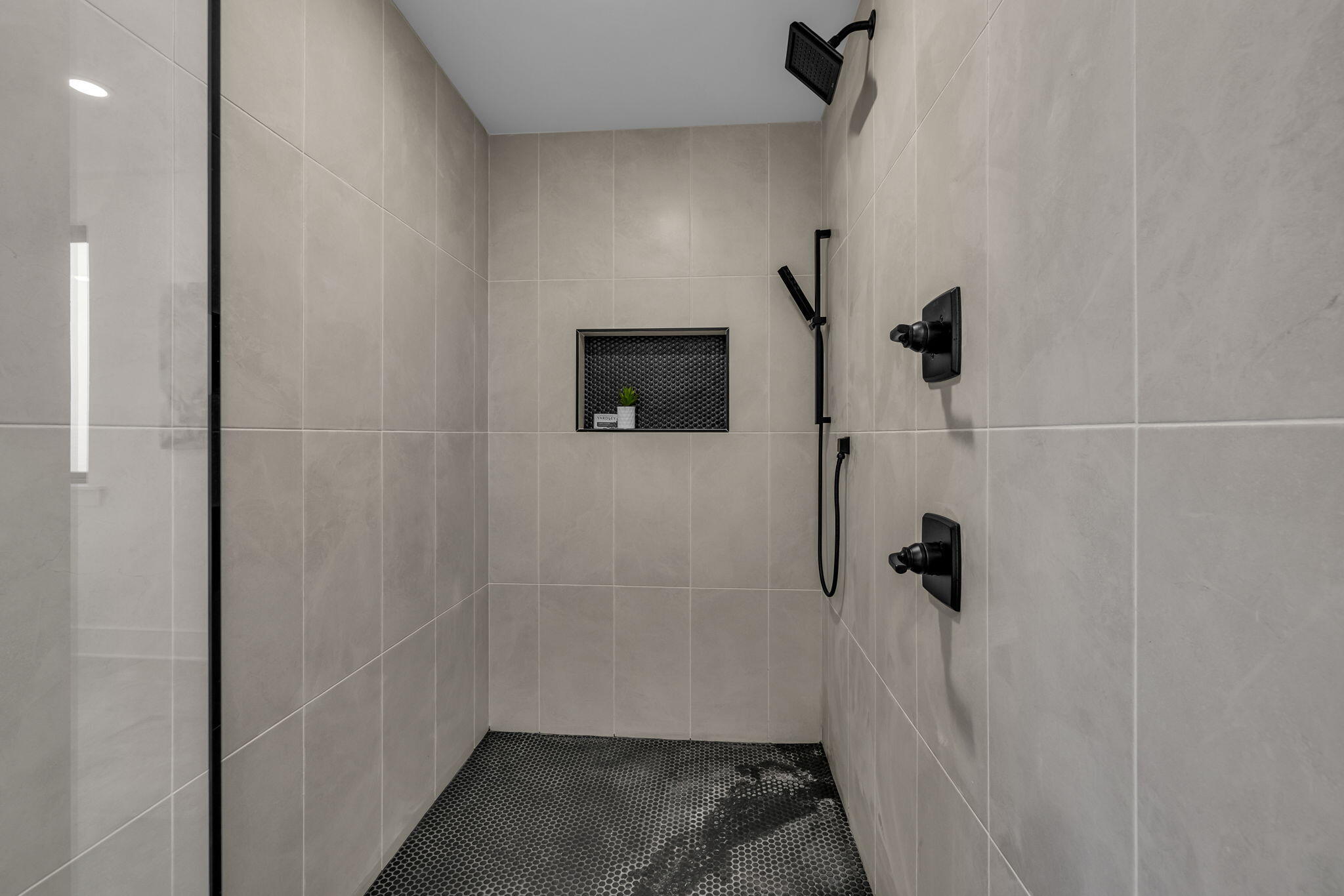 Walk-in shower with black fixtures, dark pebble-tile floor, and recessed niche.