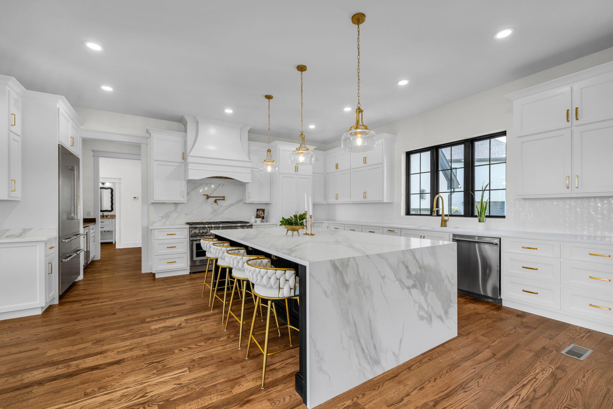 Bright white kitchen with a large marble-look island, brass pendants, and warm wood floors.