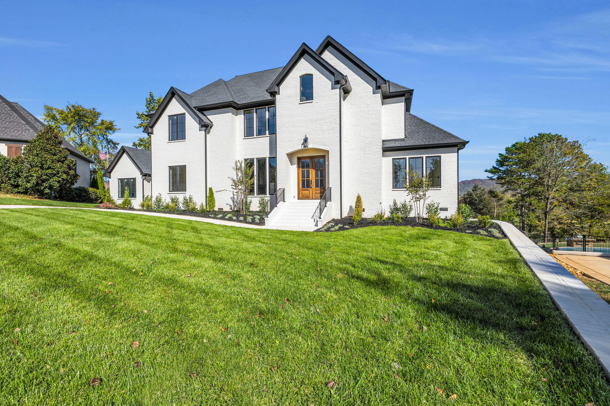 Two-story white brick home with a wooden double door, broad lawn, and pool at the side.