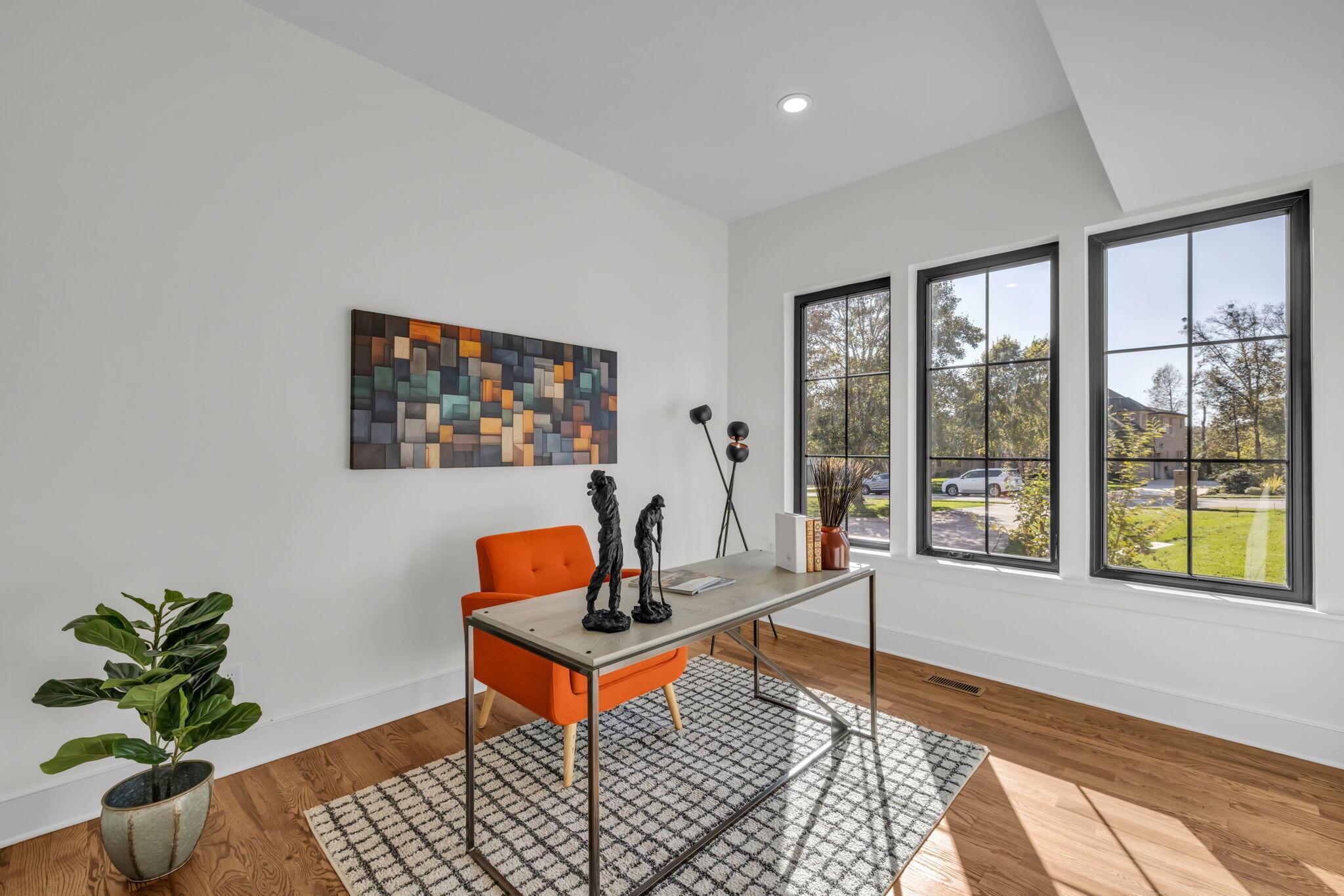 Staged home office with orange chair, geometric wall art, and three tall black-framed windows.