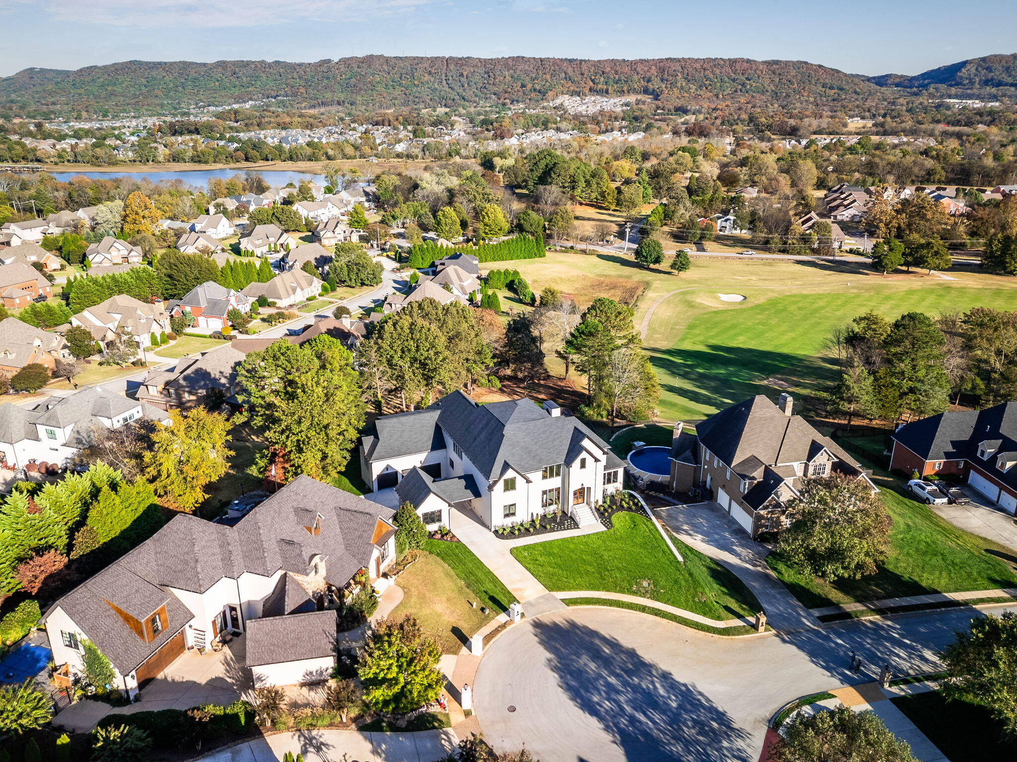 Aerial view of the home beside a golf course, with a backyard pool and wooded hills beyond.