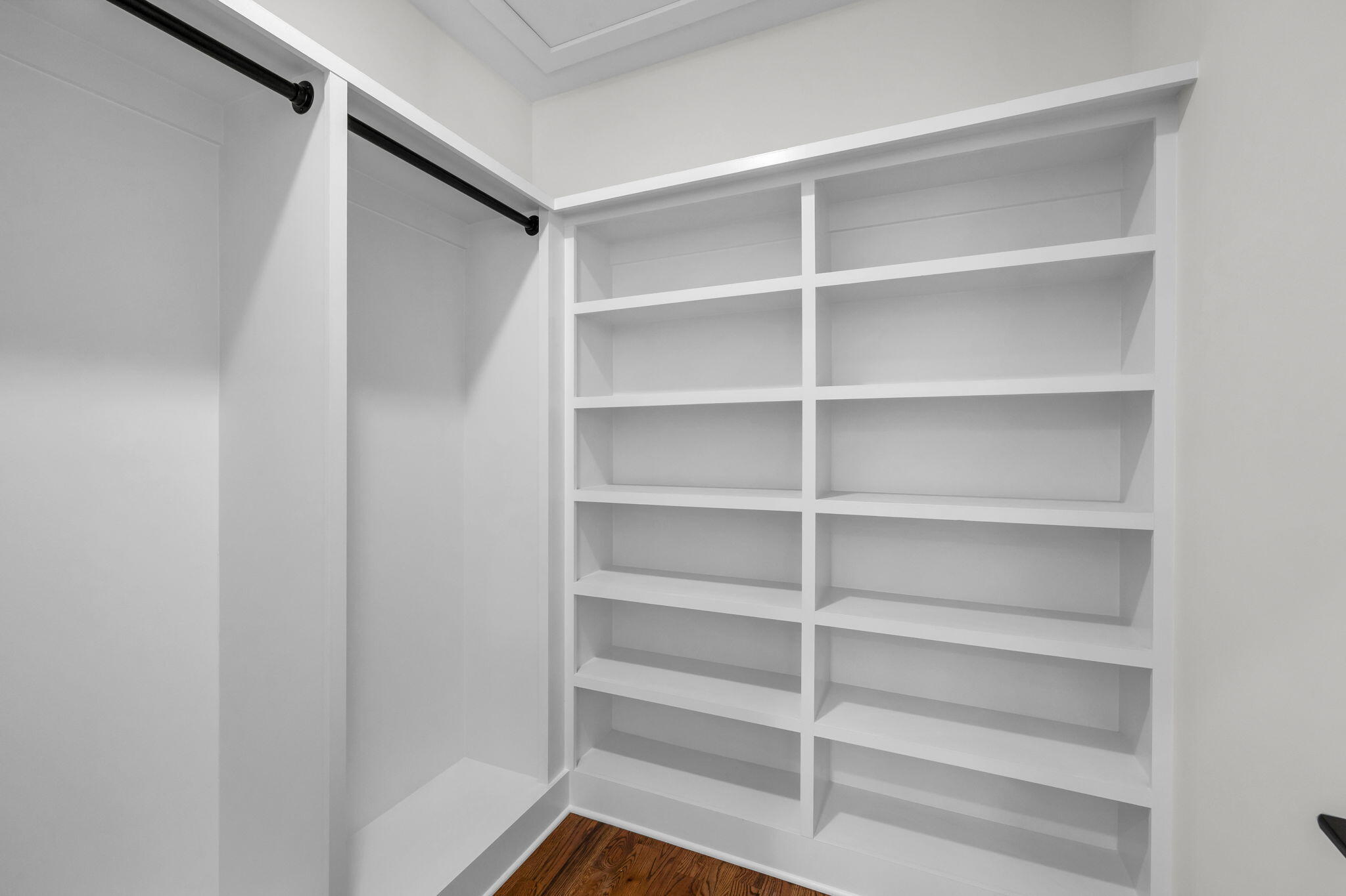 Empty walk-in closet with built-in shelves, a black hanging rod, and dark wood flooring.