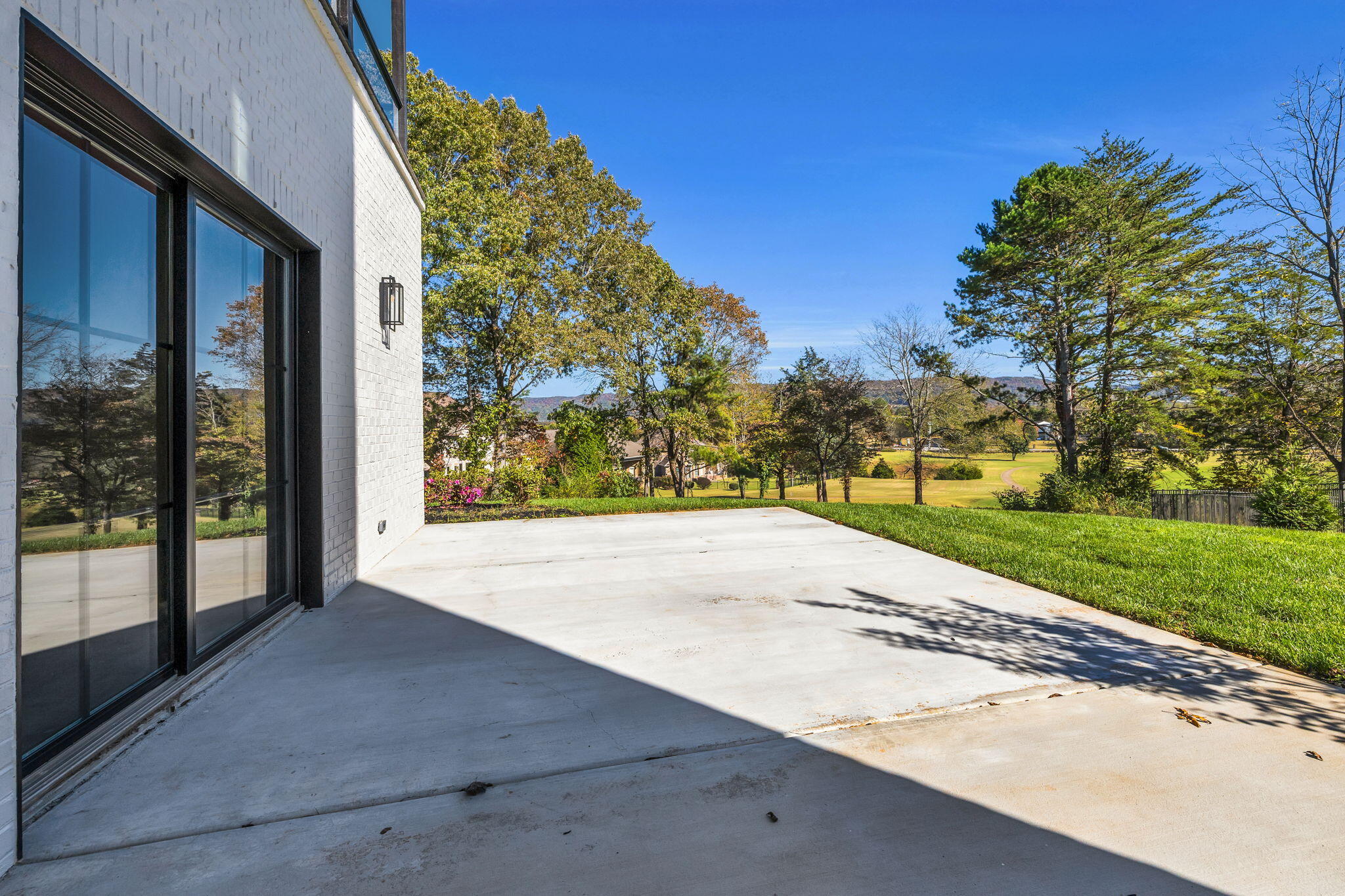 Concrete patio beside a white-brick home overlooks landscaped grounds and distant wooded hills.