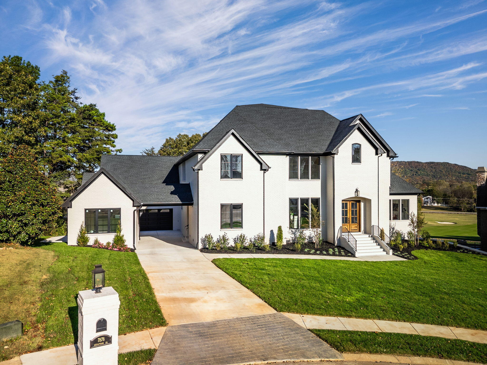Two-story white house with dark gabled roofs, a wood-and-glass entry door, and landscaped lawn.