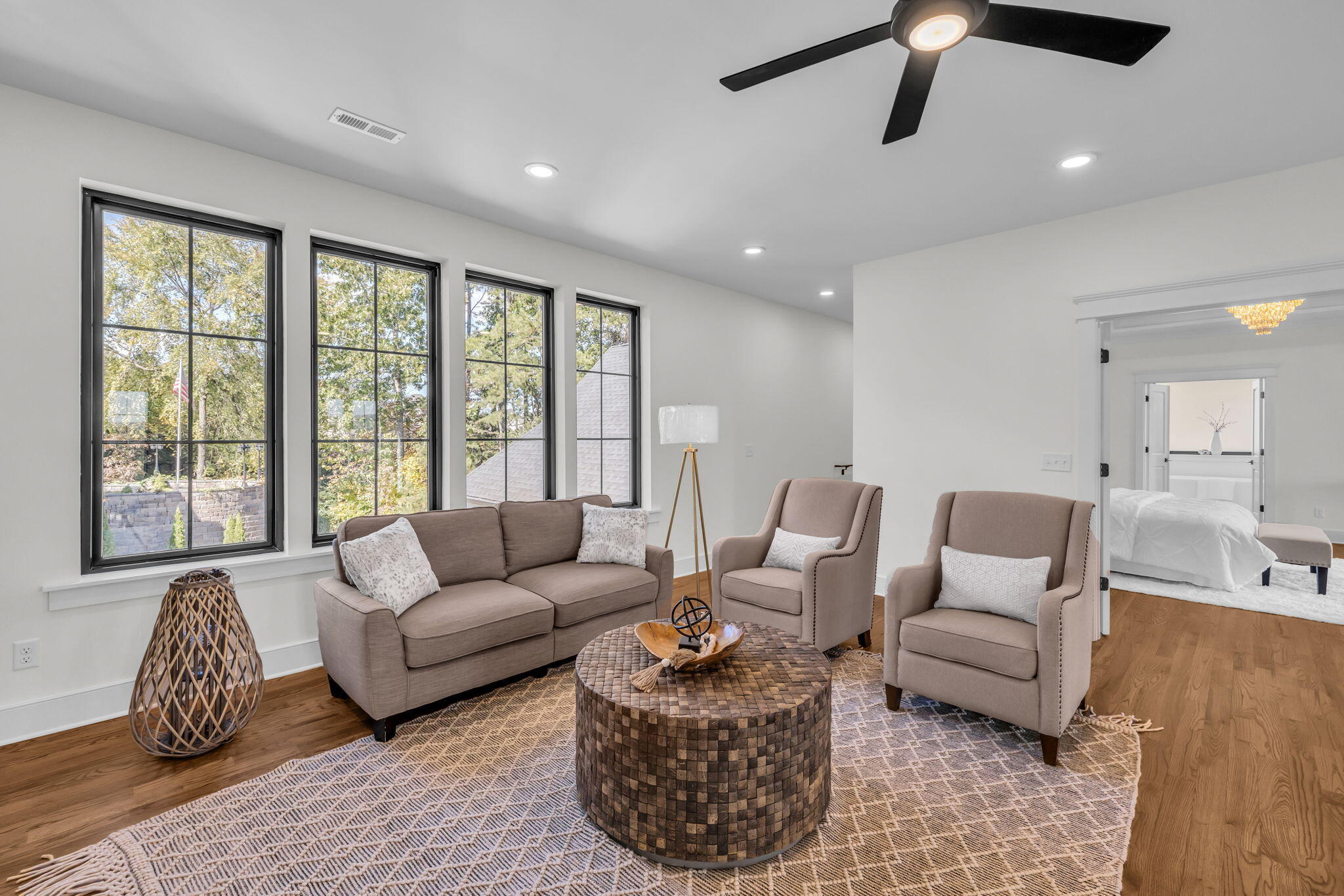 Staged living room with tall black-framed windows, a taupe sofa, and two armchairs around a woven coffee table.