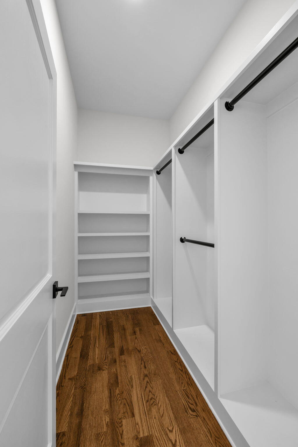 Walk-in closet with built-in shelves, black hanging rods, and hardwood floors.