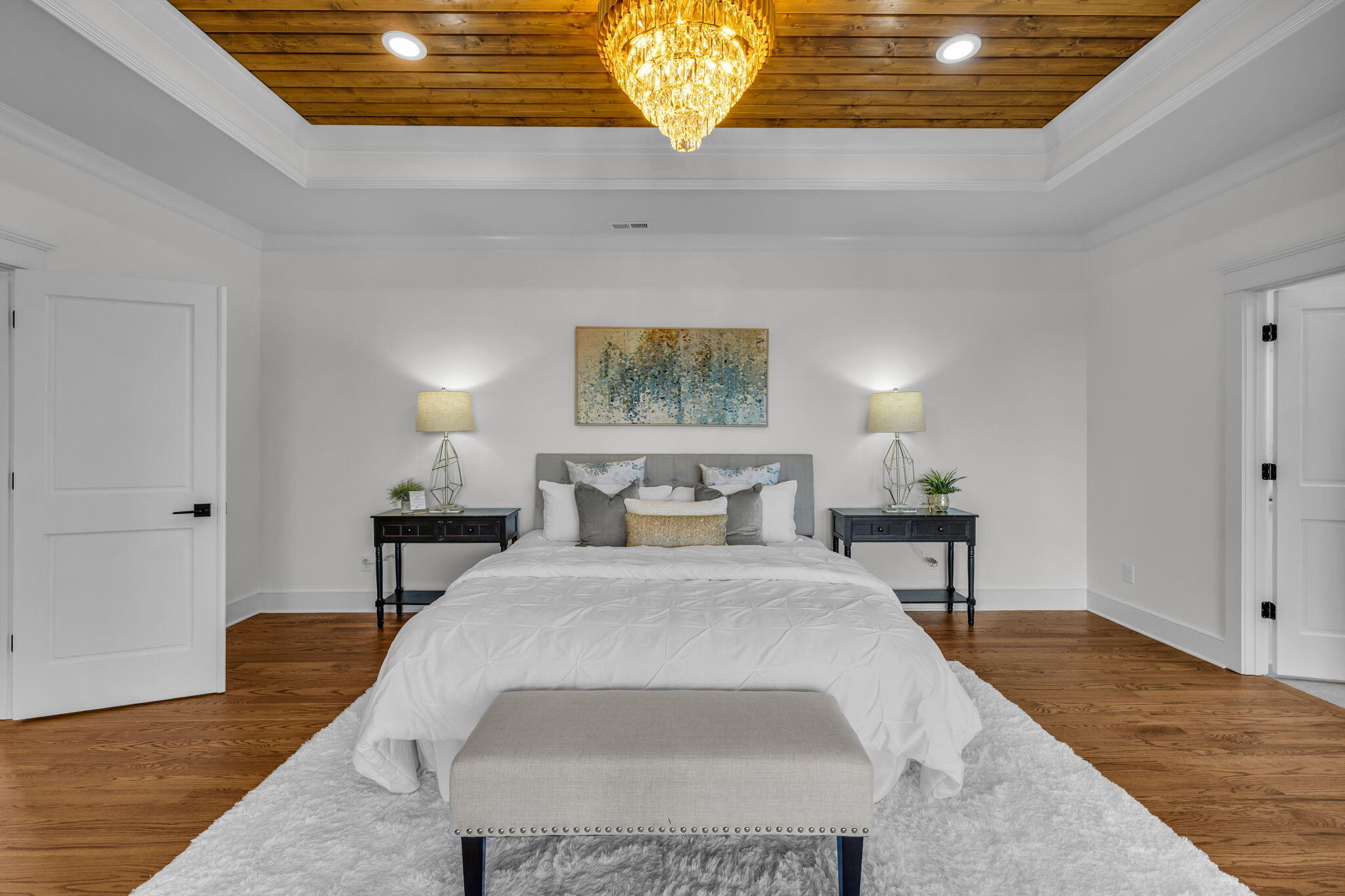 Staged bedroom with a large bed beneath a wood plank ceiling and chandelier.
