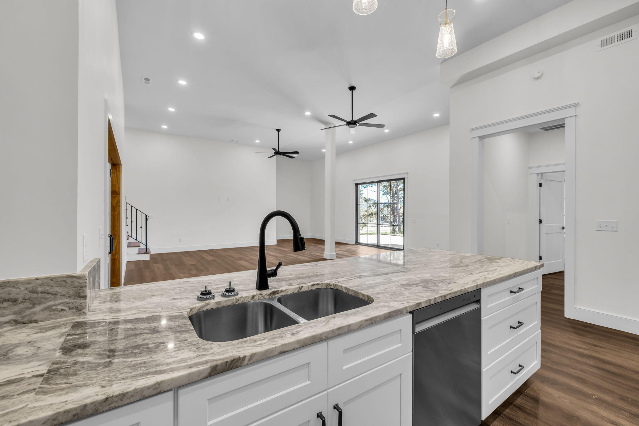 Open kitchen with a large stone island, double sink, white cabinetry, and dark wood floors.