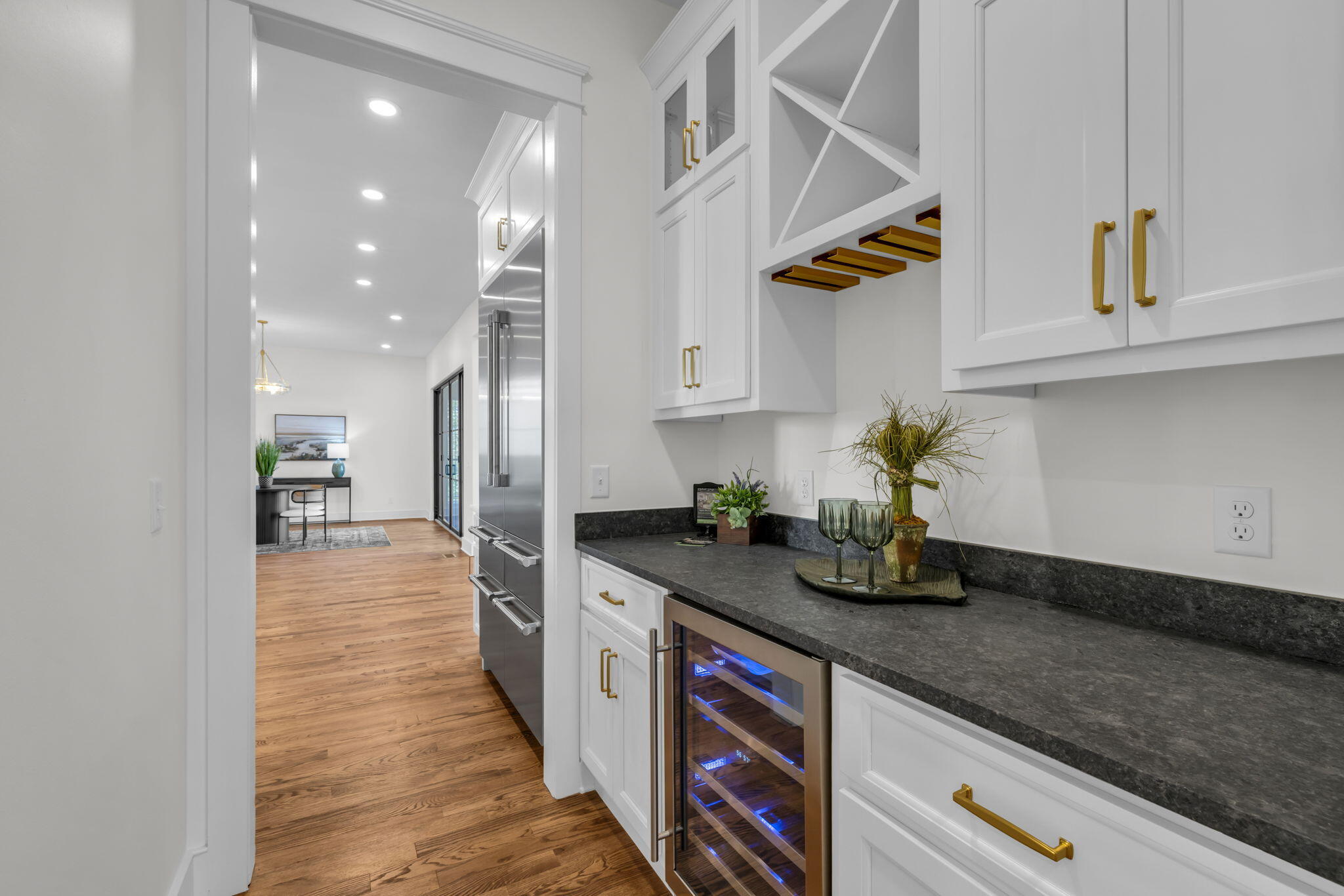 Kitchen with white cabinets, dark counters, gold hardware, and a glass-front wine refrigerator.