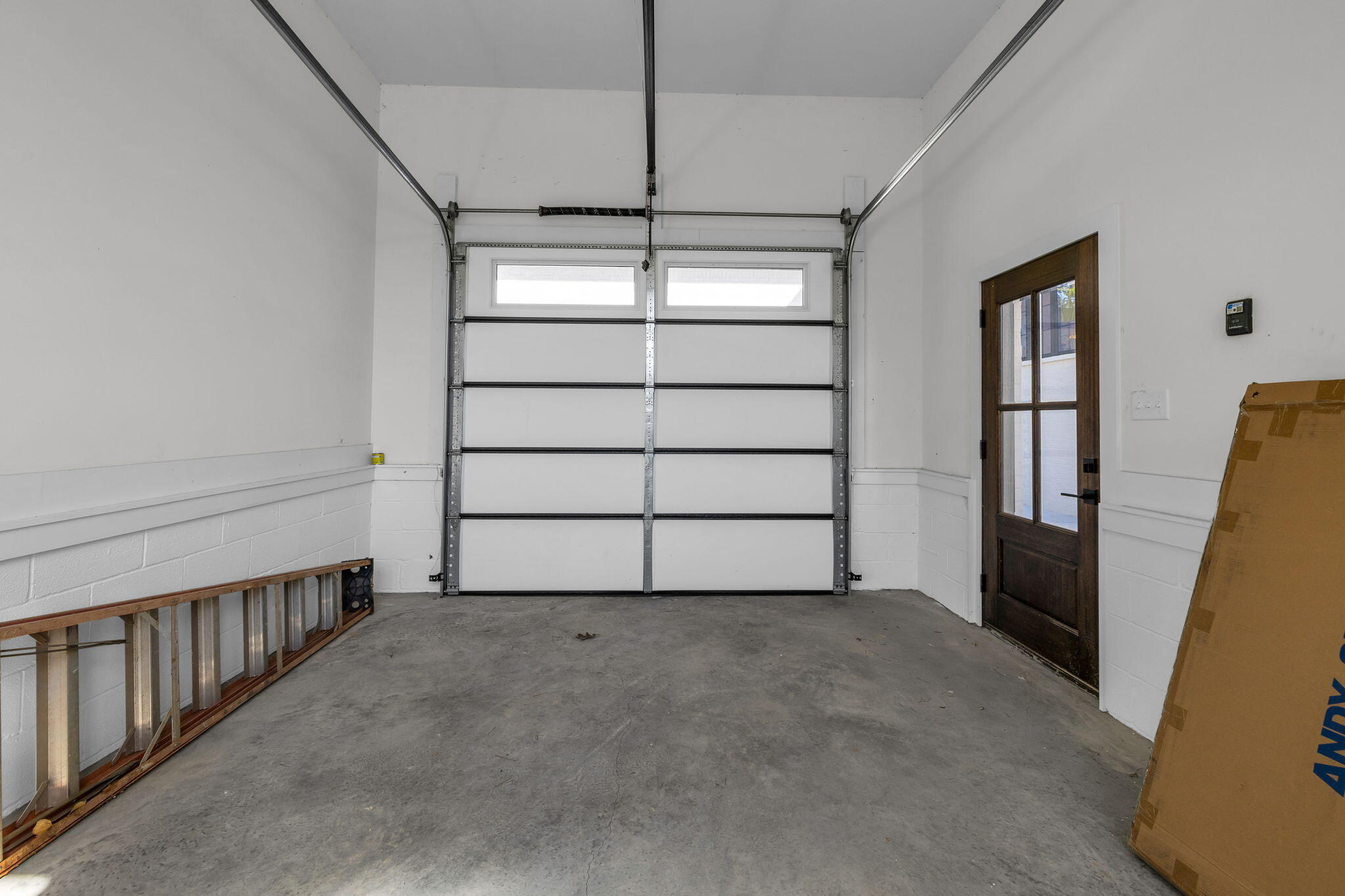 Garage with a closed overhead door, concrete floor, and dark wood side-entry door.
