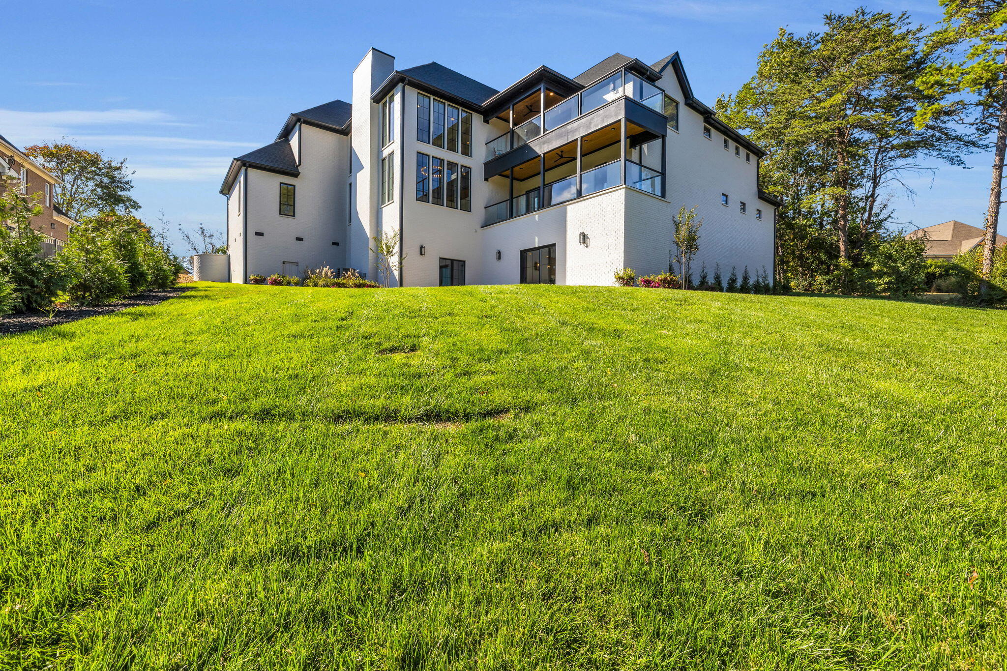 Modern white-brick house with glass balconies above a broad sloping lawn.