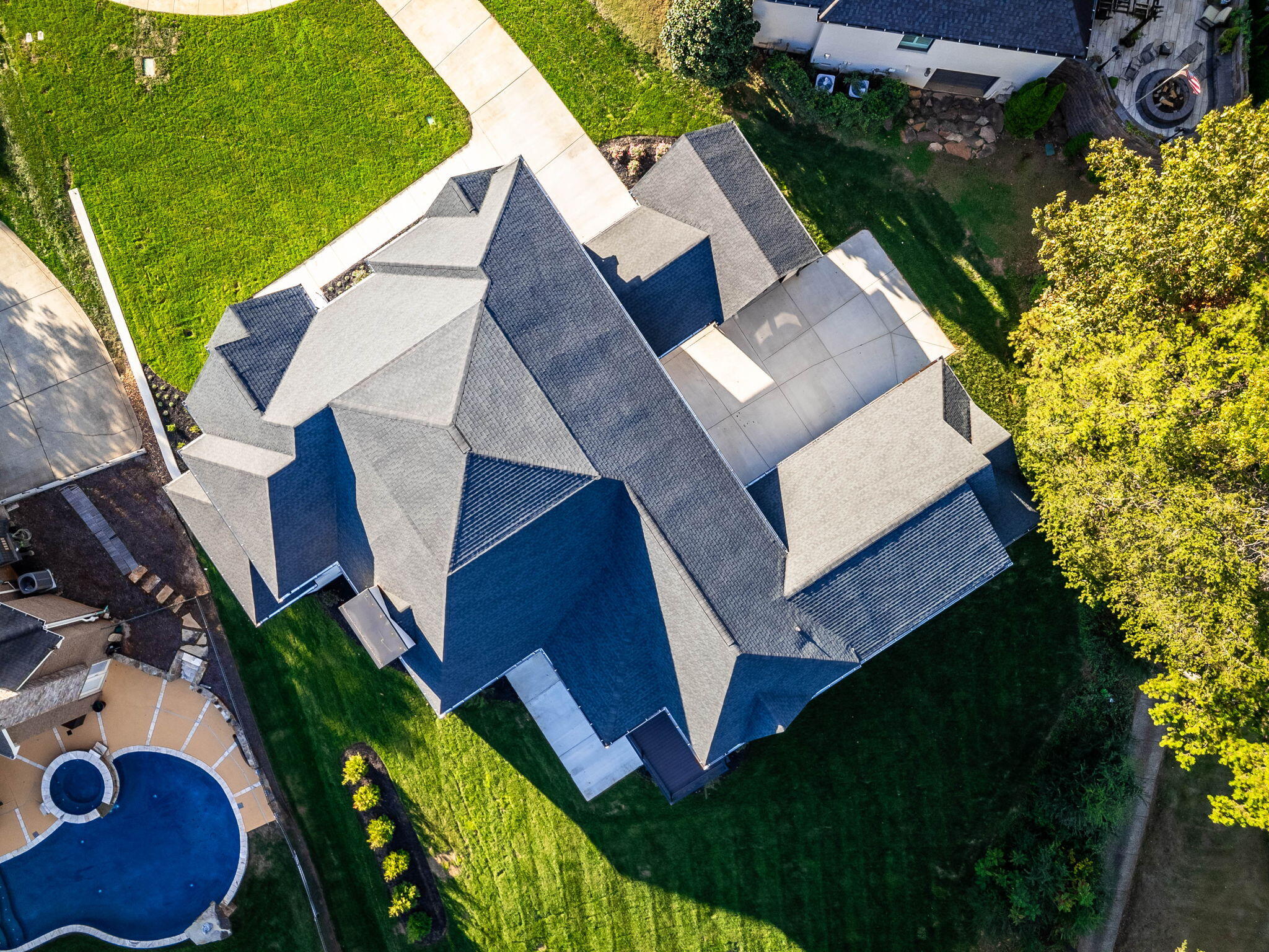 Aerial view of a large gray-roofed home, green lawn, paved driveway, and curved swimming pool.