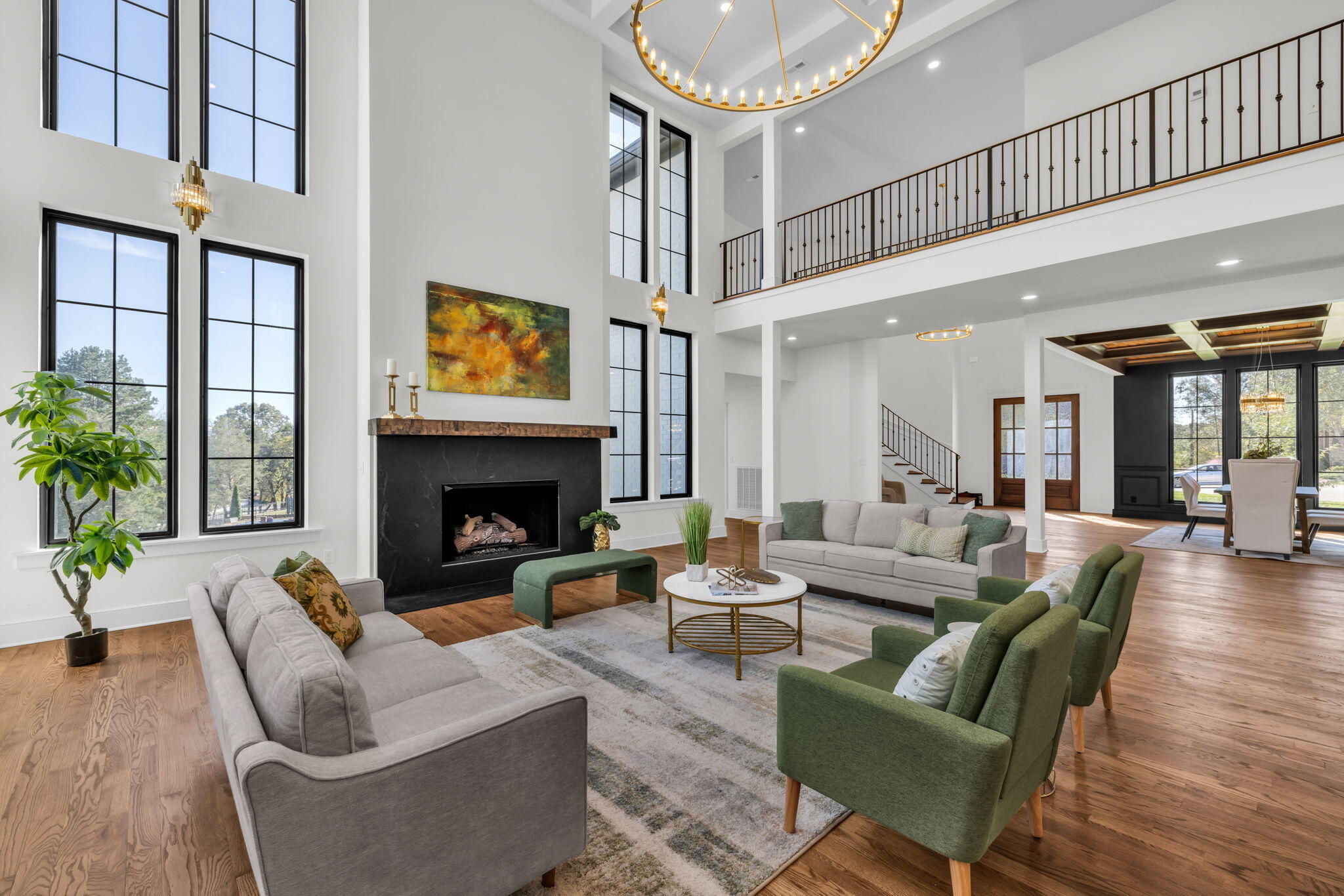 Furnished double-height living room with tall black-framed windows, fireplace, and open mezzanine.