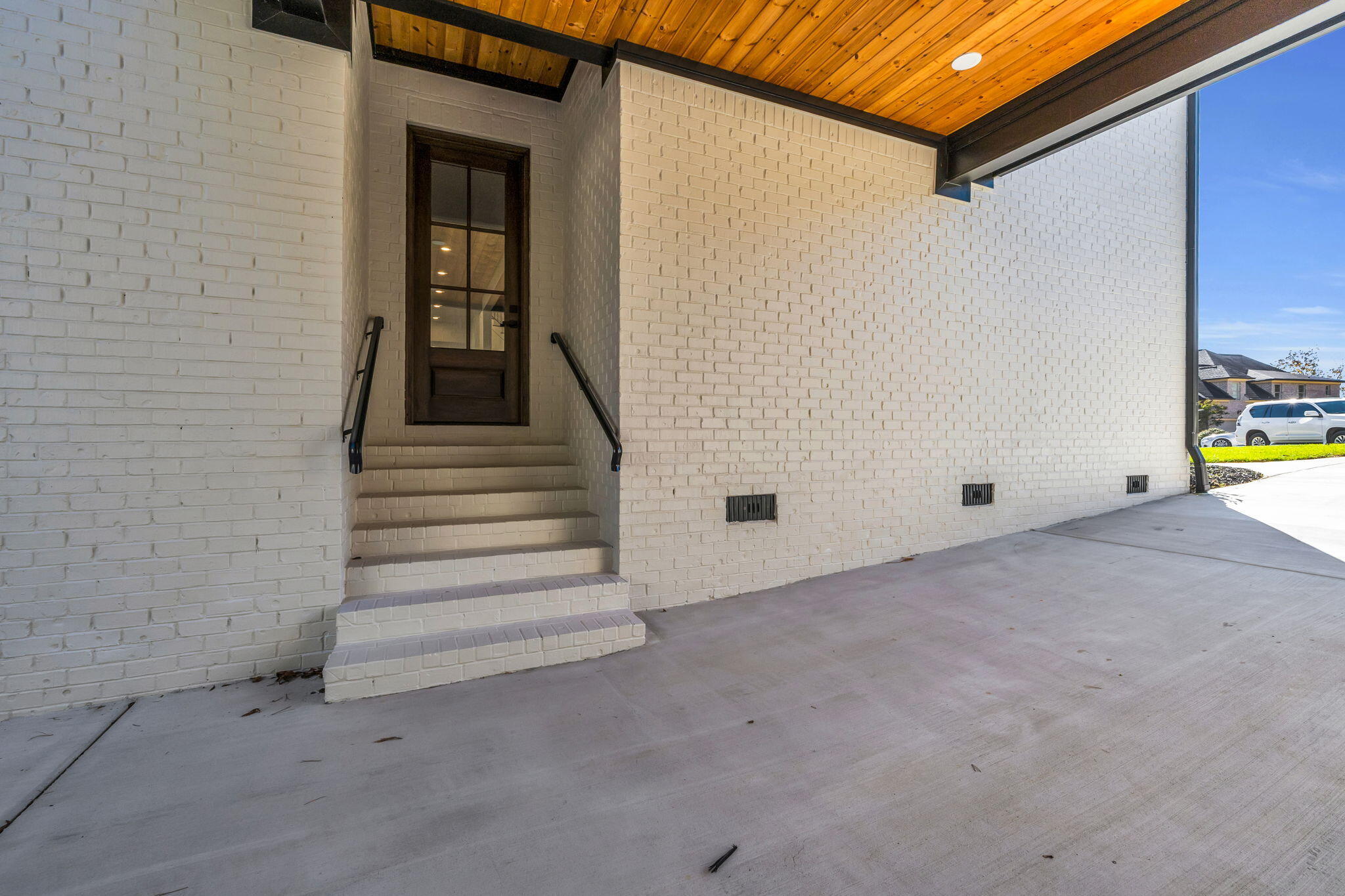 White brick covered entry with brick steps, a dark wood door, and a wood-plank ceiling.